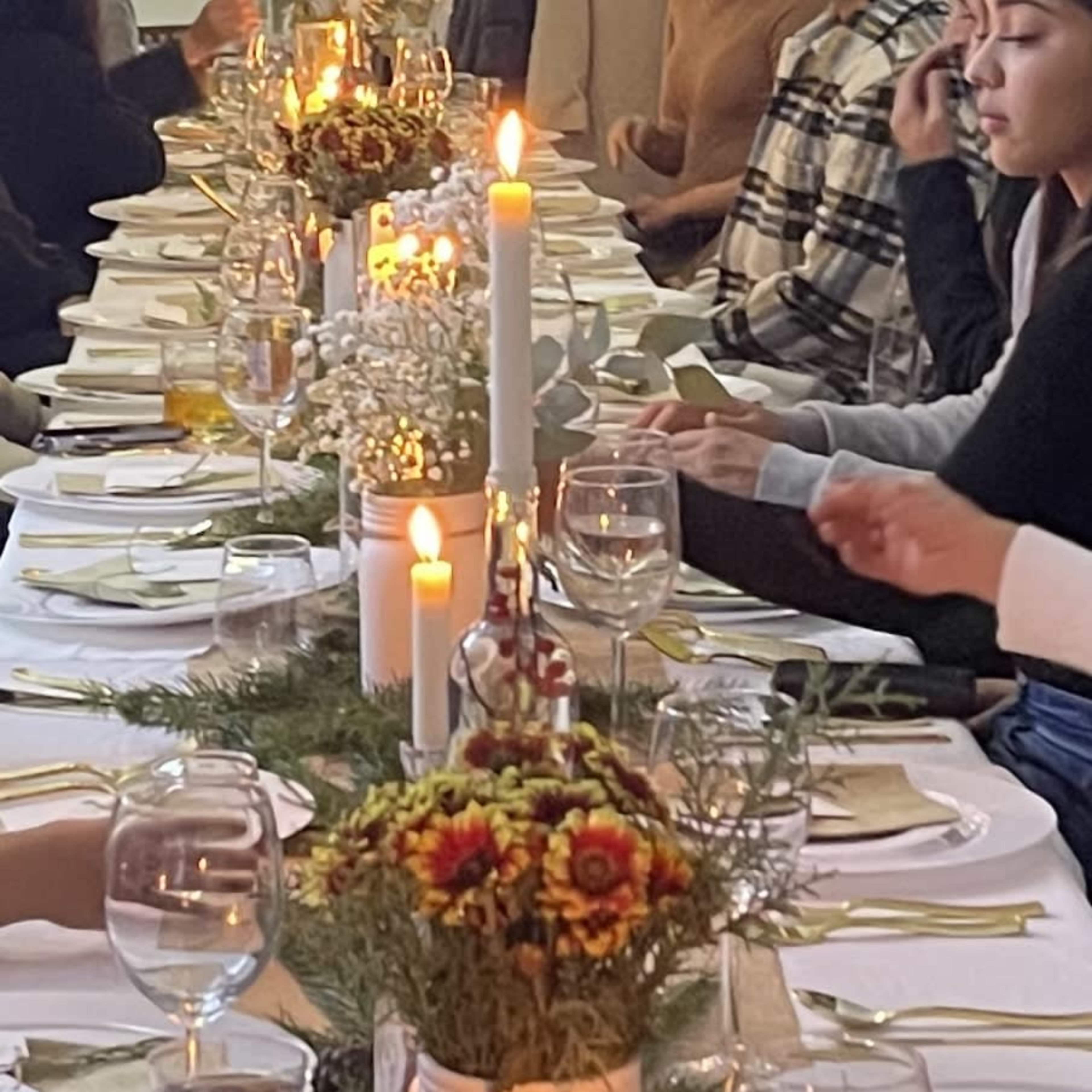 A long dining table is set with plates, glasses, and candles, decorated with flowers and greenery.