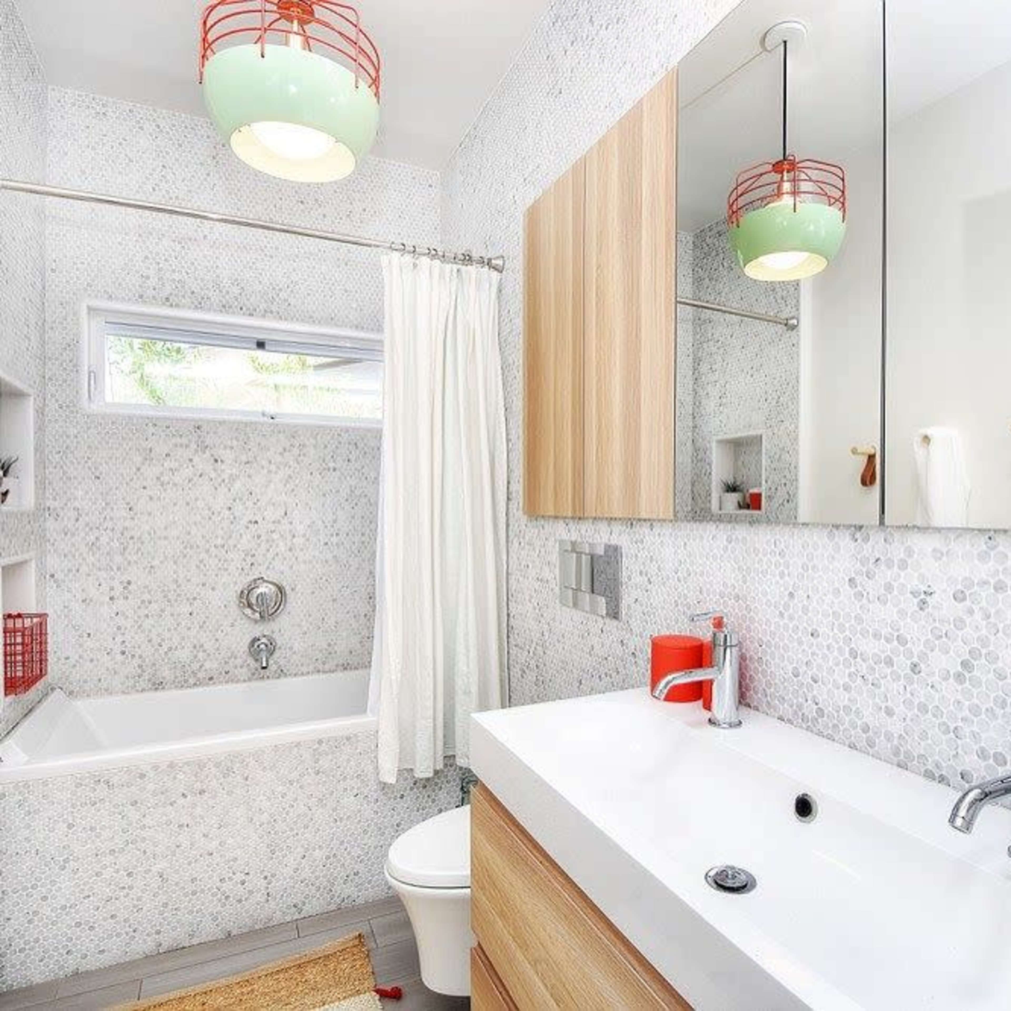 A modern bathroom featuring a bathtub, a wooden vanity with a sink, a mirror, and light fixtures, complemented by mosaic-tiled walls and a potted plant.