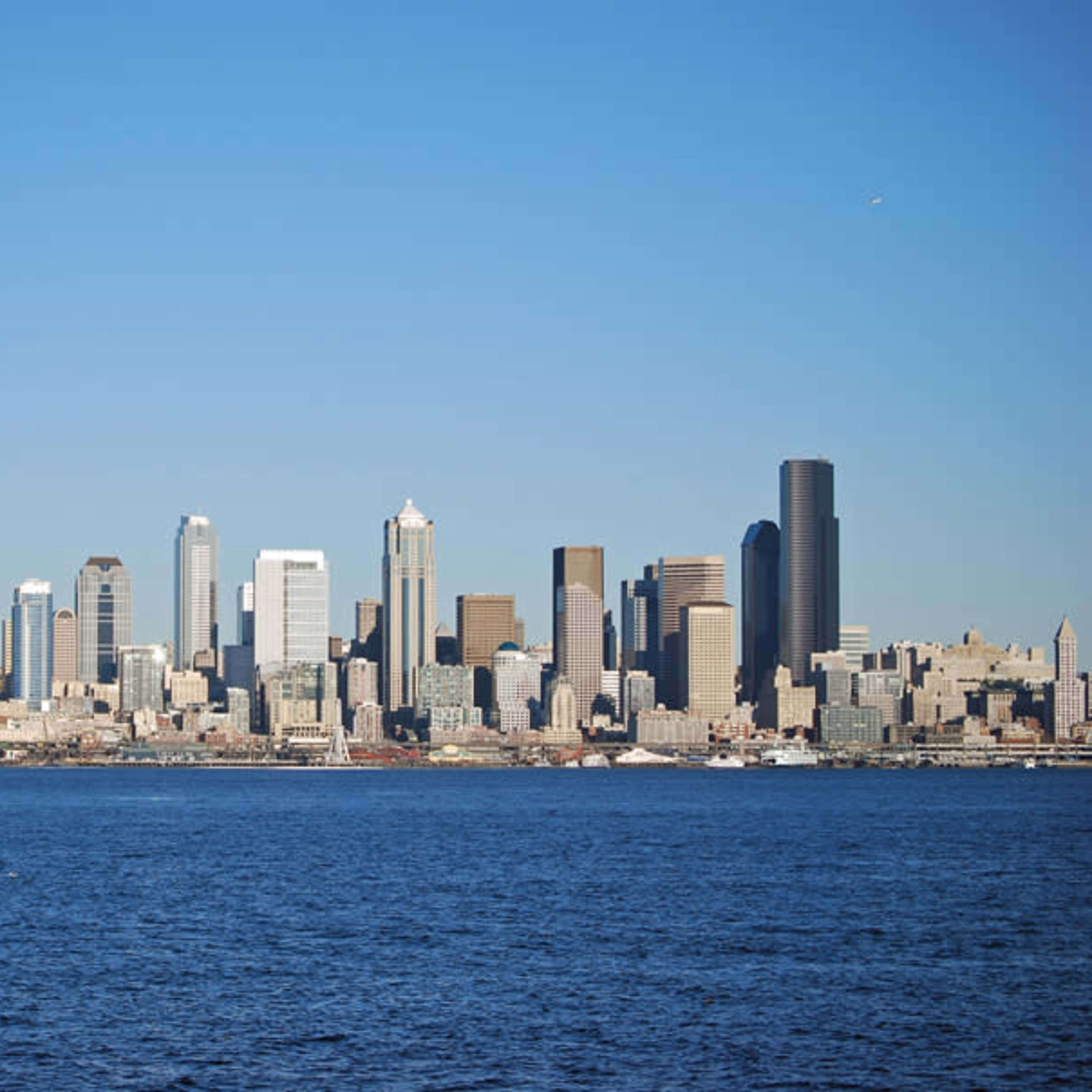 A skyline of tall buildings along a waterfront with a ferry in the foreground.