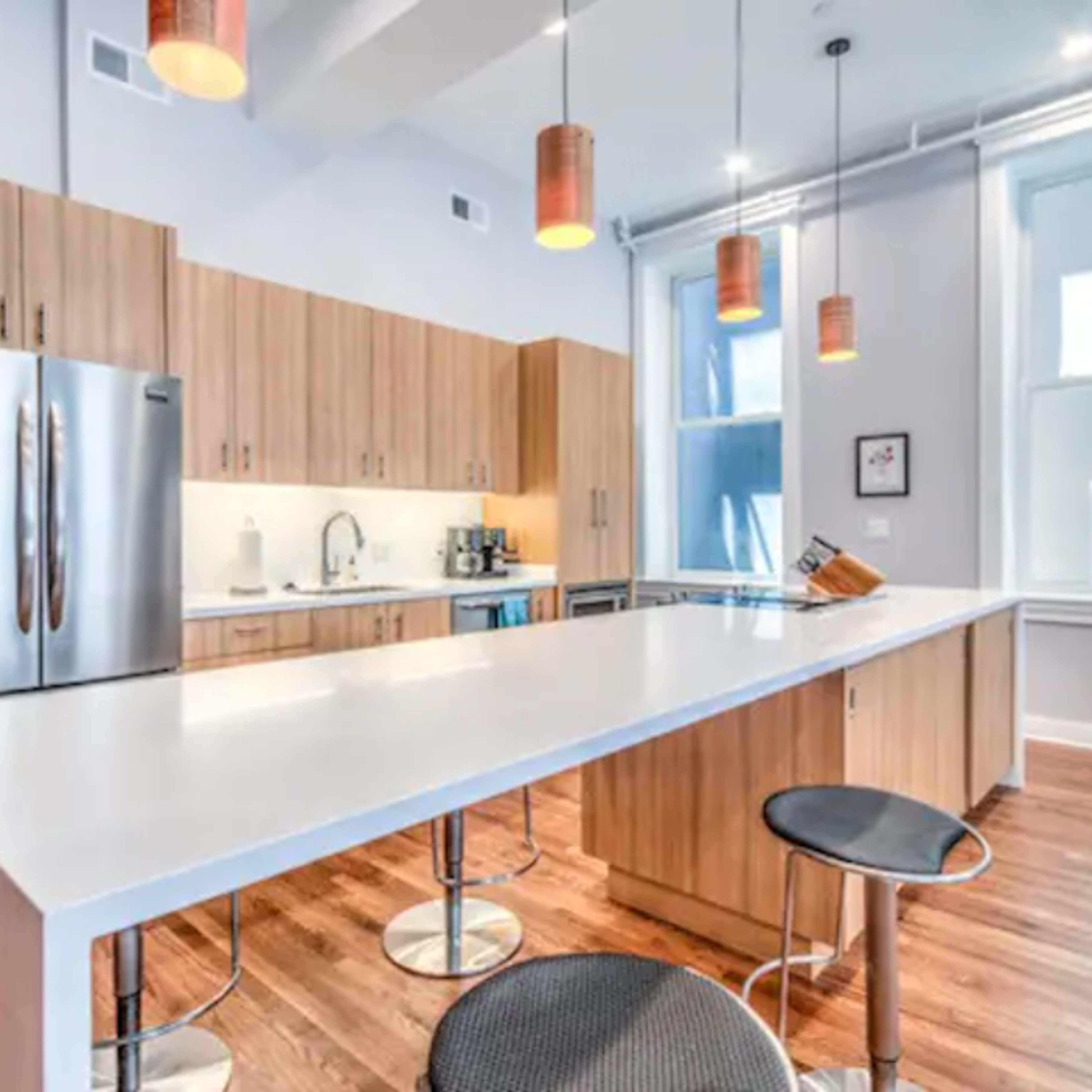 A modern kitchen with wooden cabinetry, stainless steel appliances, a large central island, and pendant lighting.