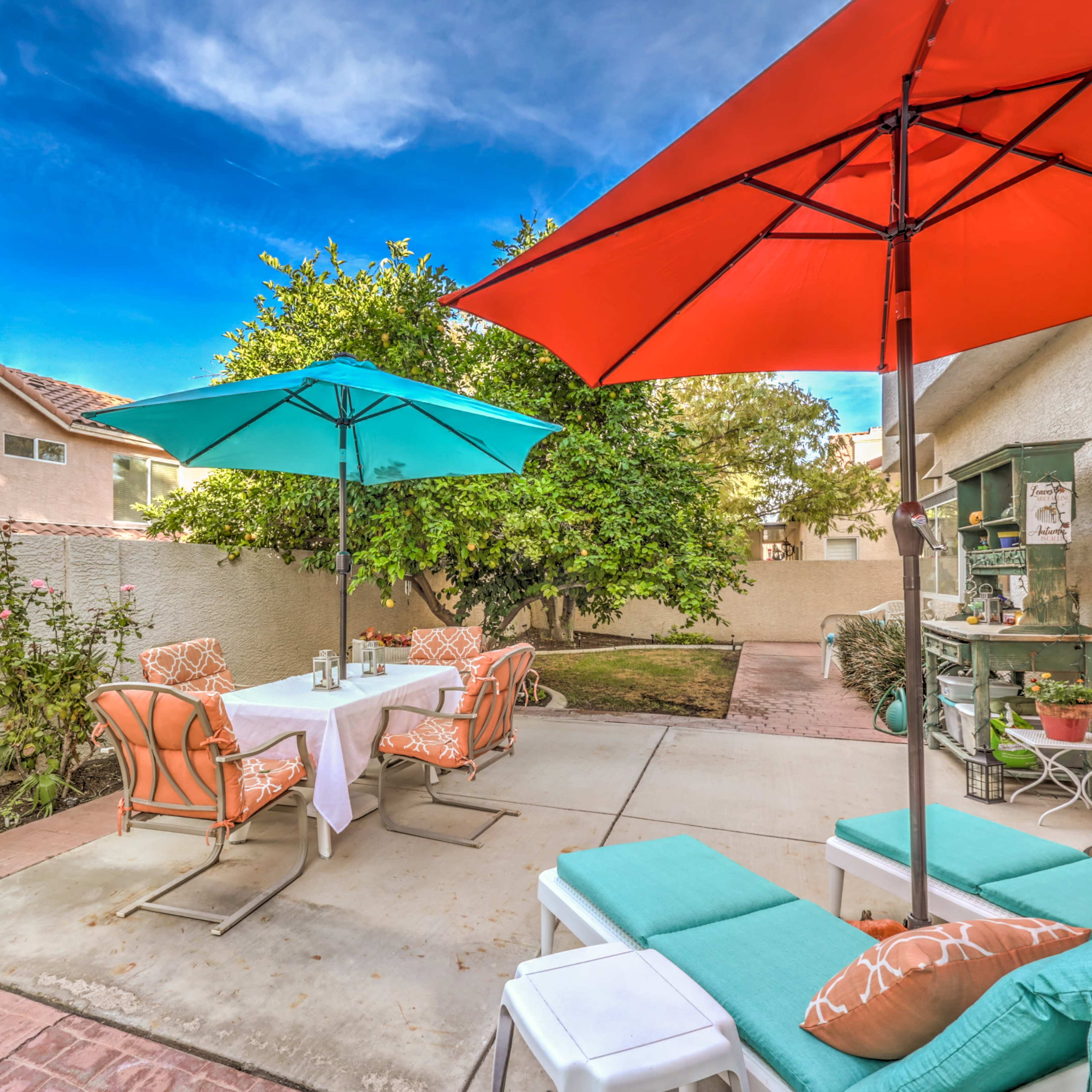 A backyard scene with a table set for outdoor dining, surrounded by colorful umbrellas and lounge furniture.