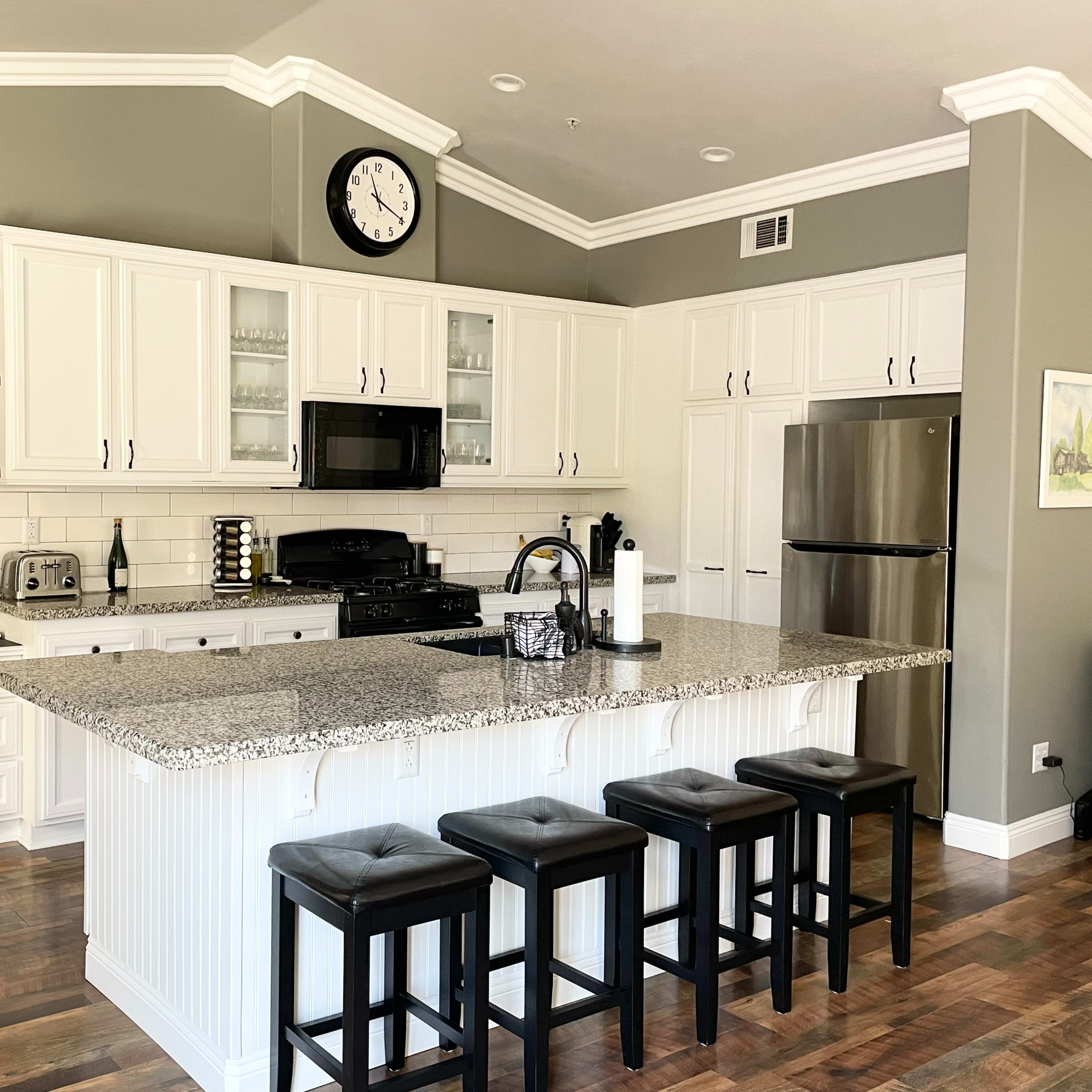 A modern kitchen with white cabinetry, a large island with seating, and stainless steel appliances.