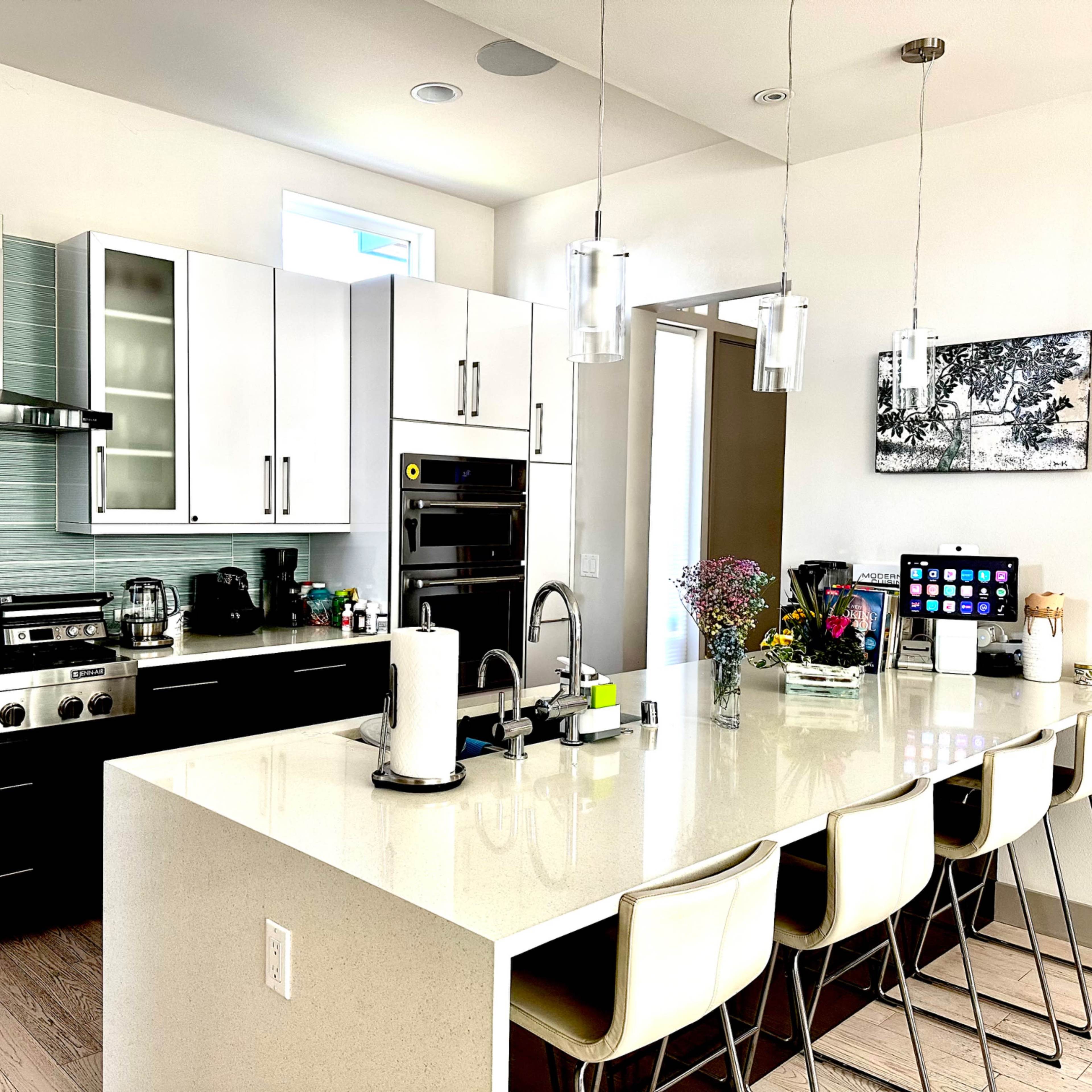 The kitchen features a modern design with a large island, stainless steel appliances, white cabinets, and a variety of countertop items.