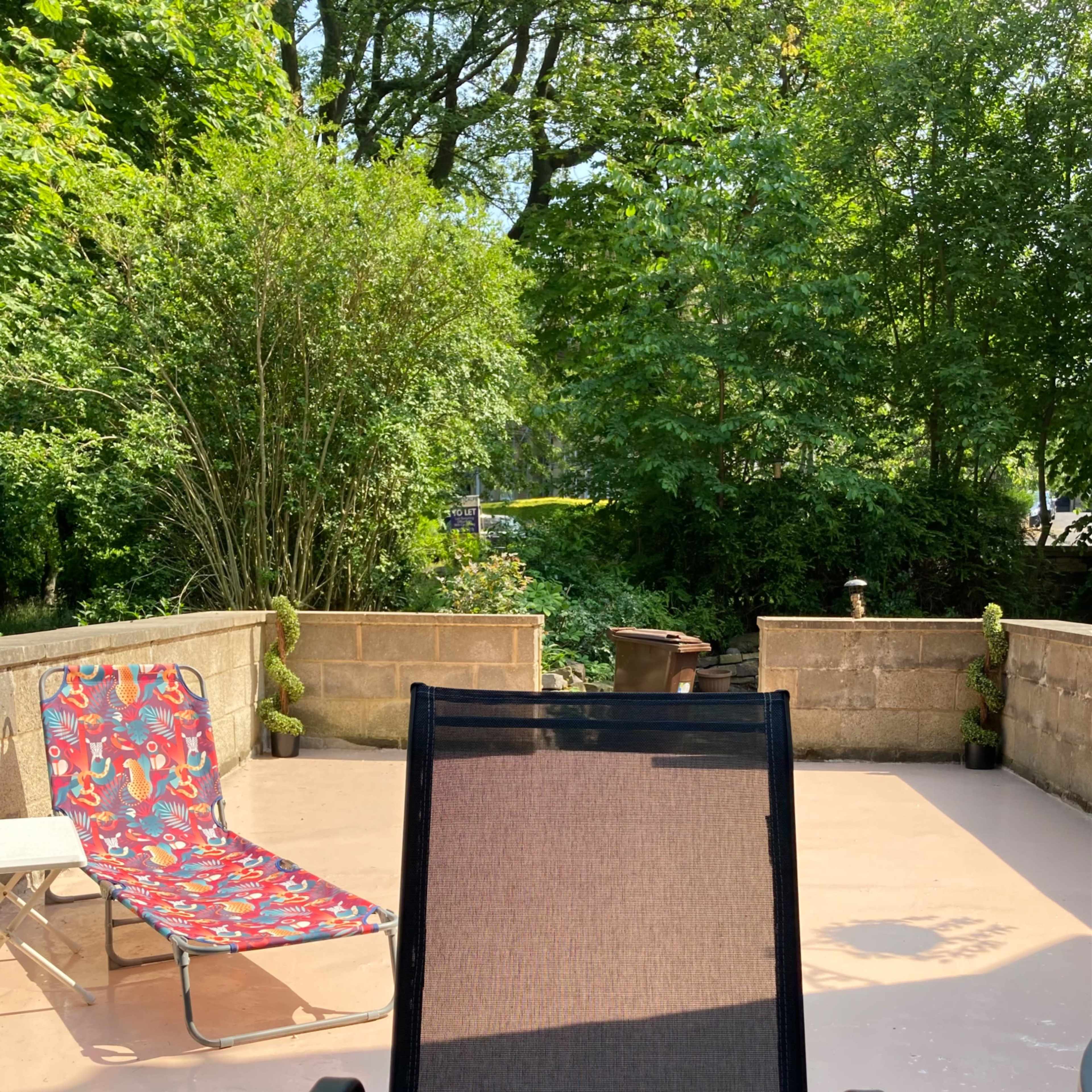 A person relaxes in a black lounge chair on a patio surrounded by greenery and a small stream.