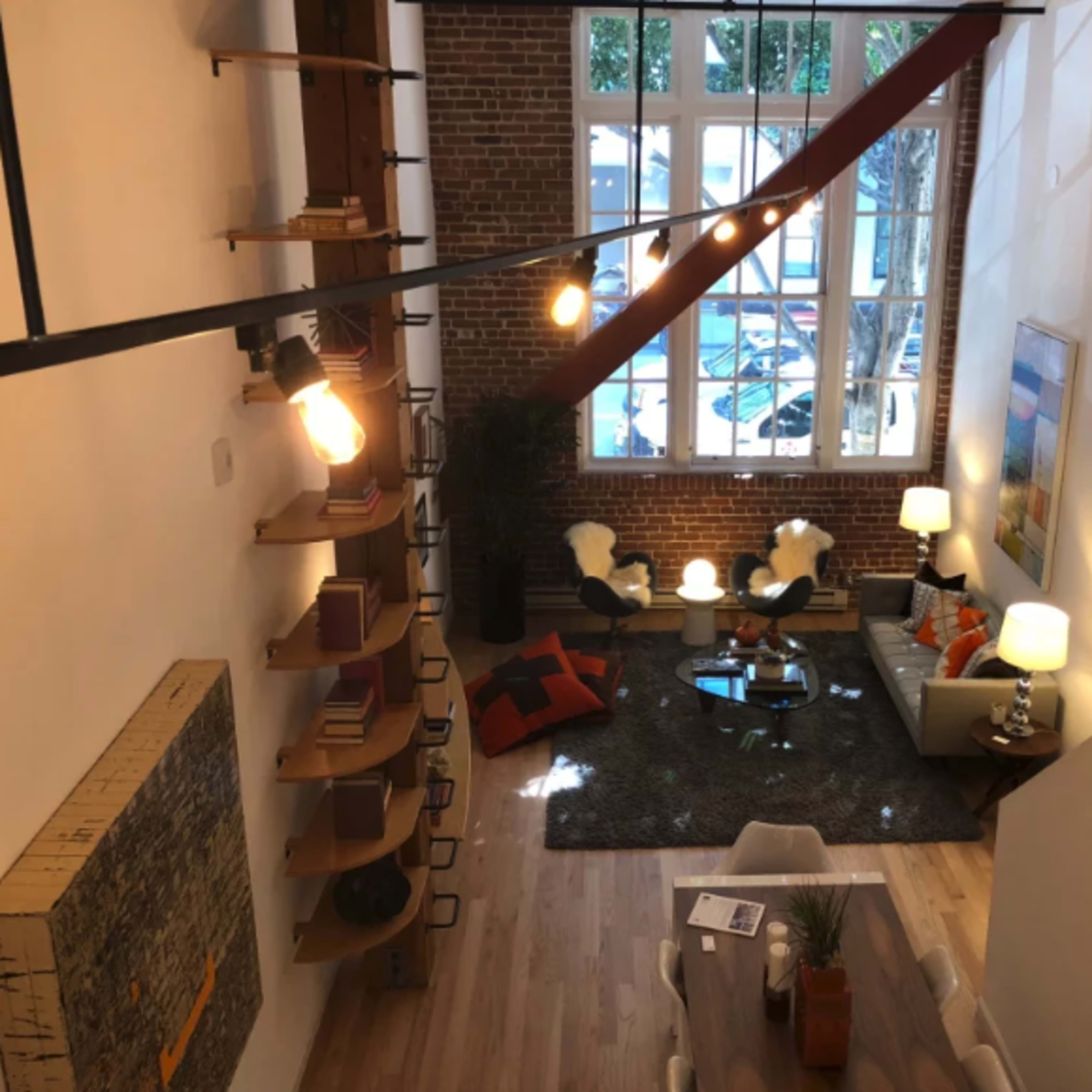 A modern living room features large windows, exposed brick walls, and contemporary furniture arranged around a central coffee table.