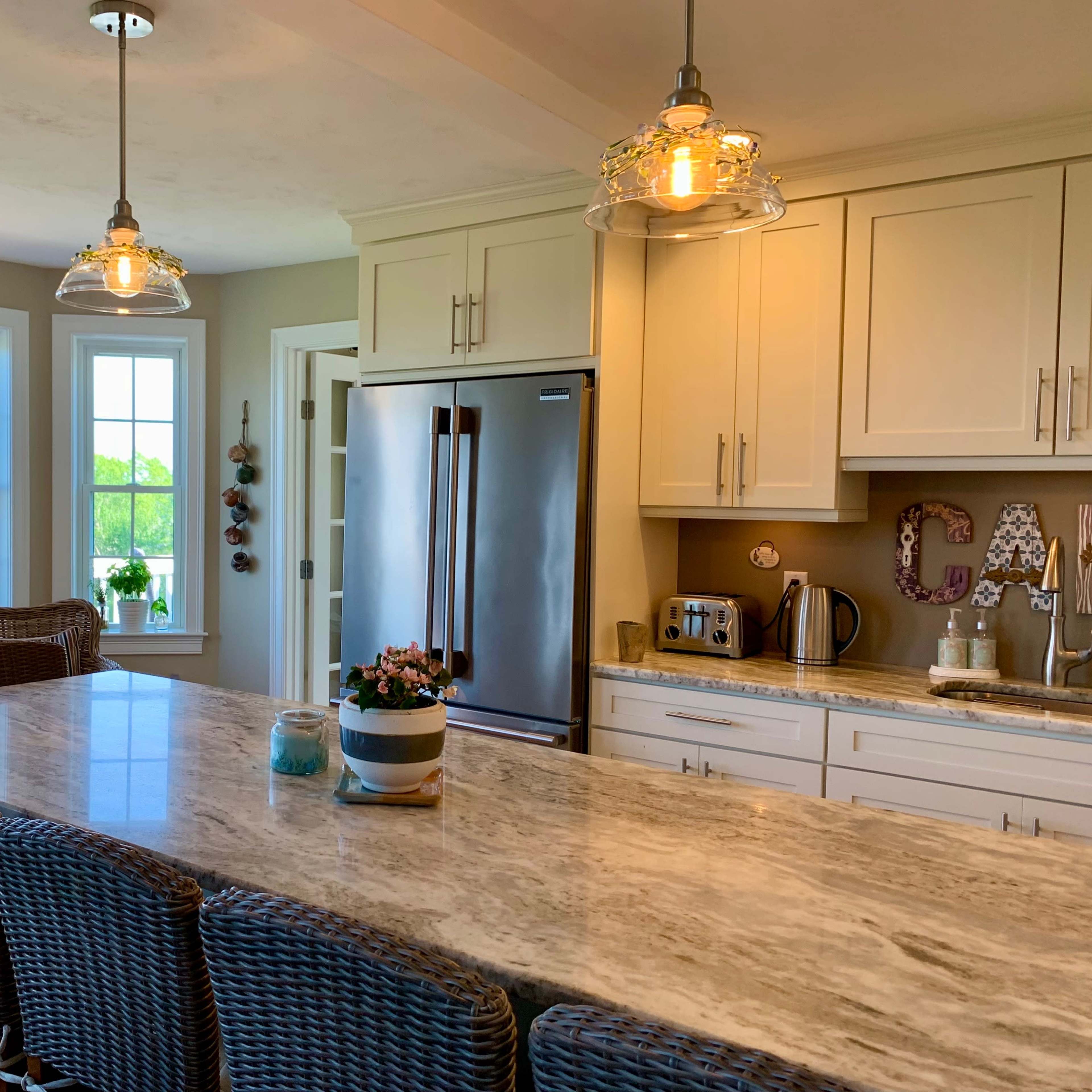 A modern kitchen features a large marble countertop with bar seating, stainless steel appliances, and abundant natural light from multiple windows.