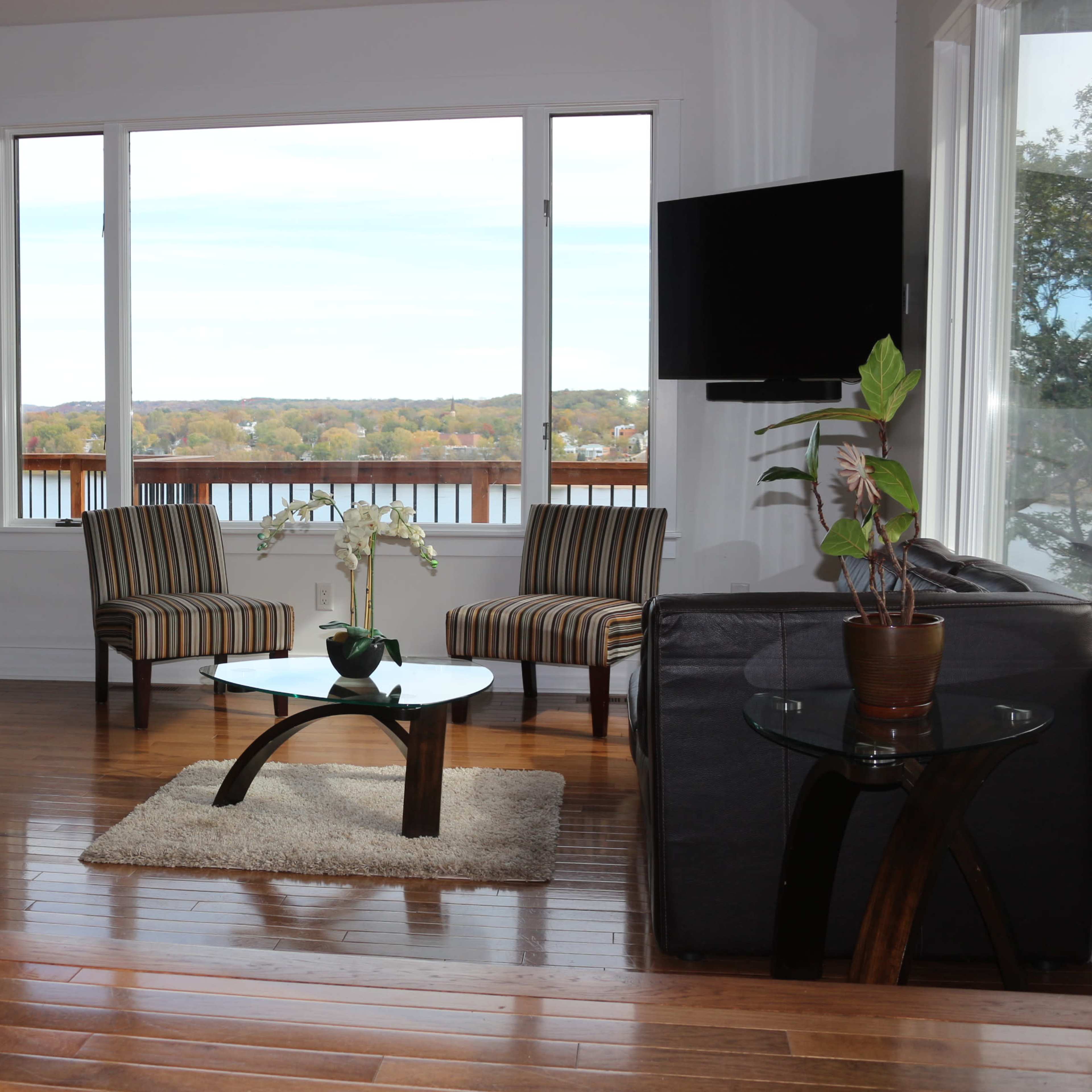 A living room with two striped chairs, a glass coffee table, and large windows overlooking a lake.