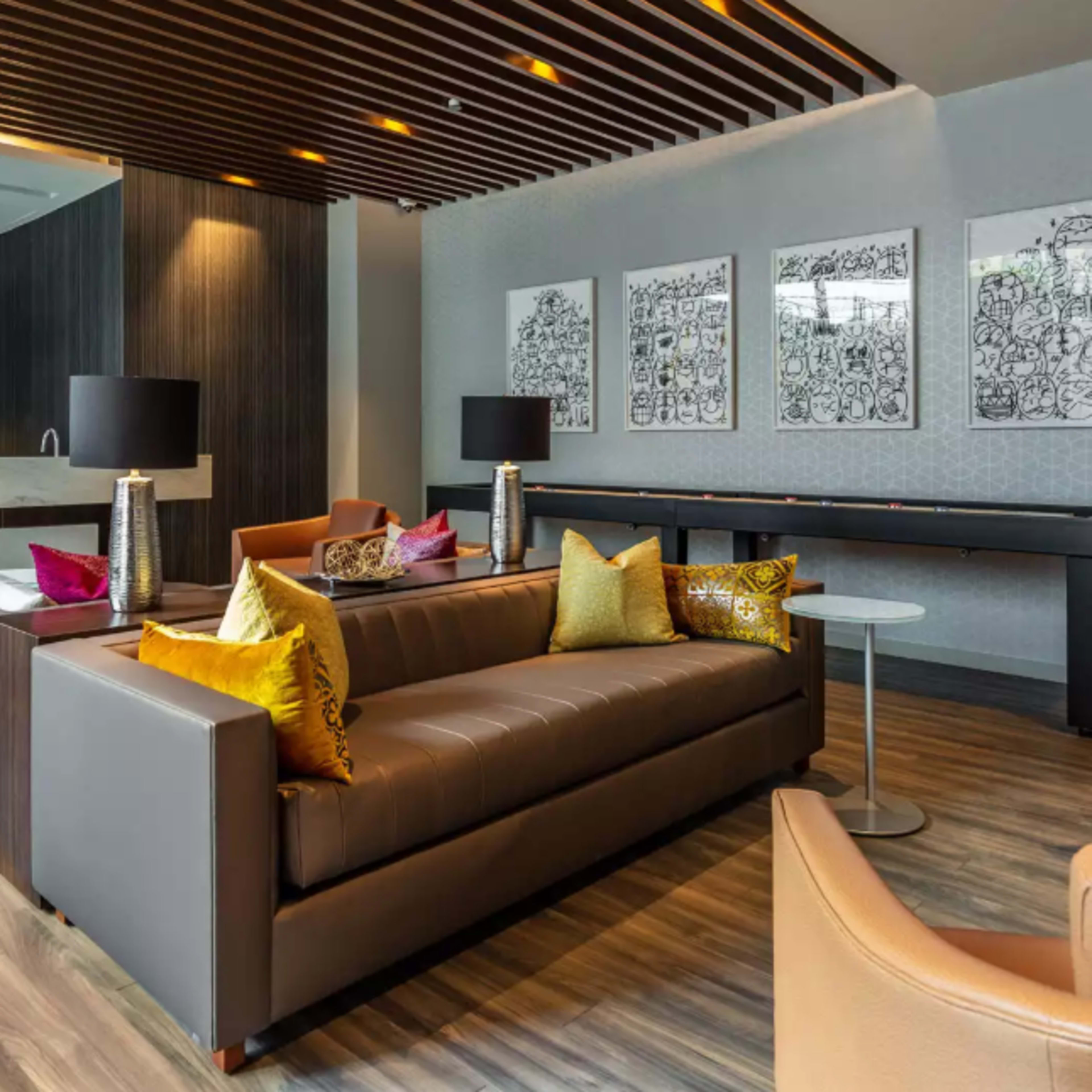 A modern lounge area with a gray sofa, colorful pillows, artwork on the walls, and a large television mounted above a marble surface.