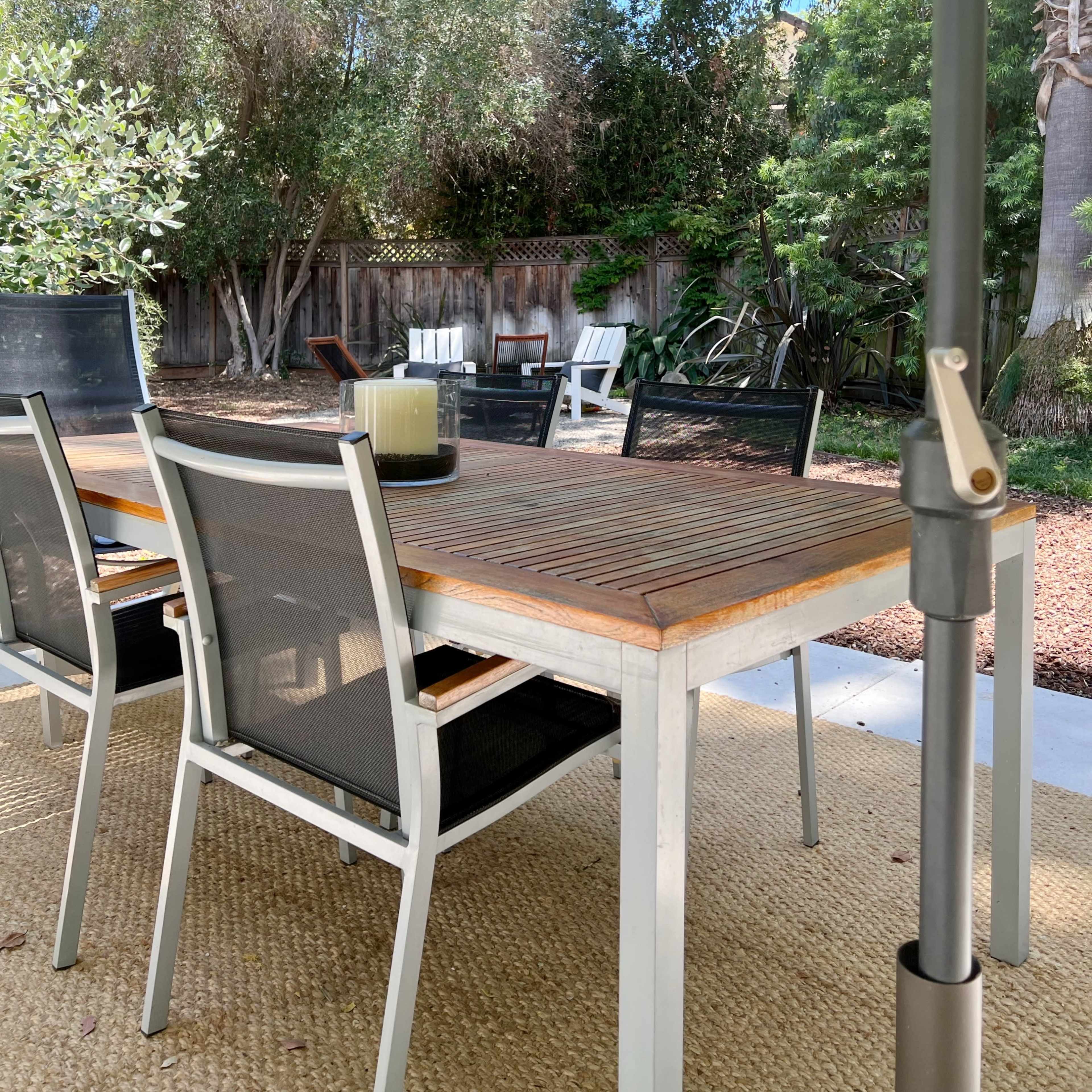 A patio table with chairs is set under an umbrella, overlooking a garden with seating areas and lush greenery.