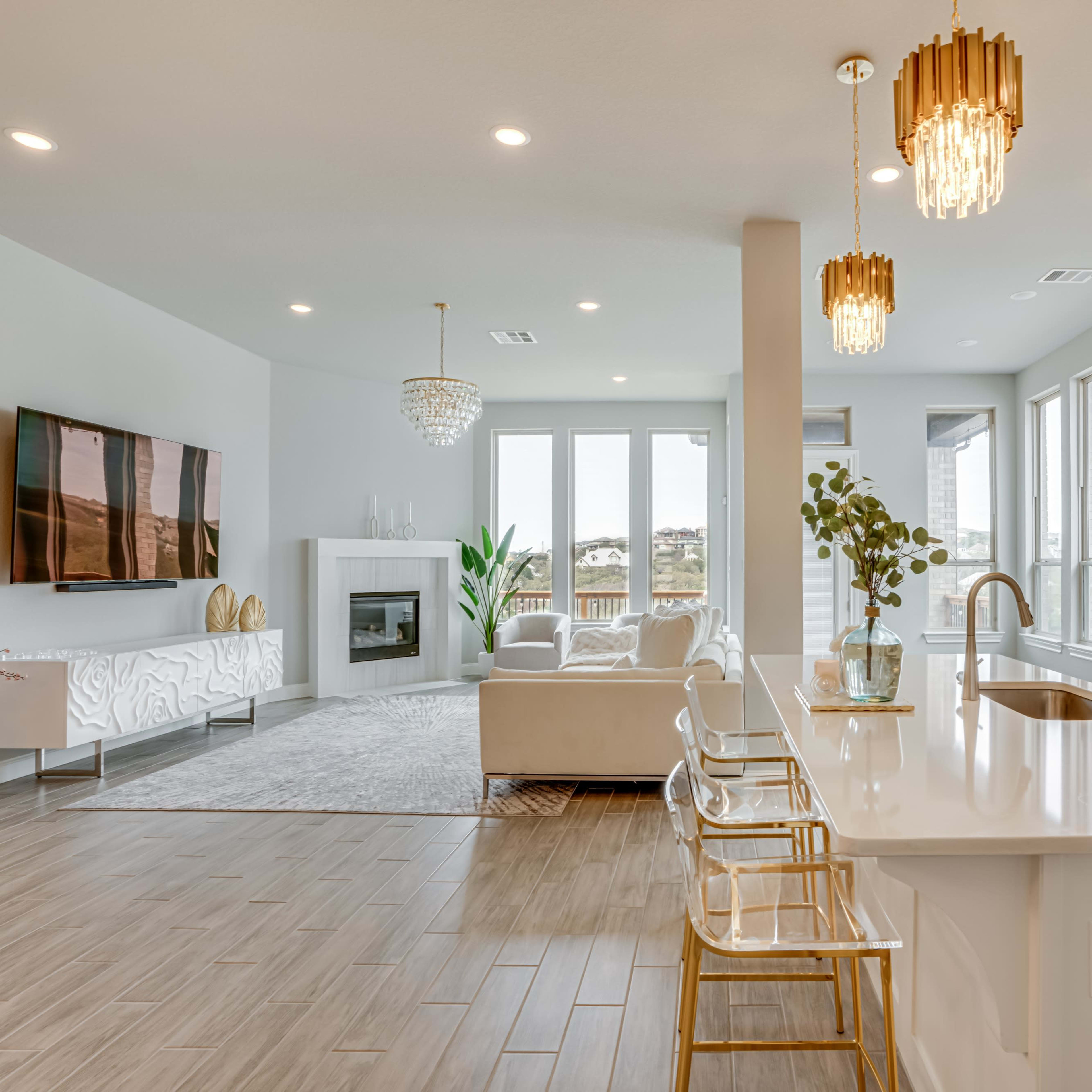 A modern open-concept living space featuring a kitchen with white cabinetry, a dining area with clear chairs, and a comfortable sitting area with large windows.
