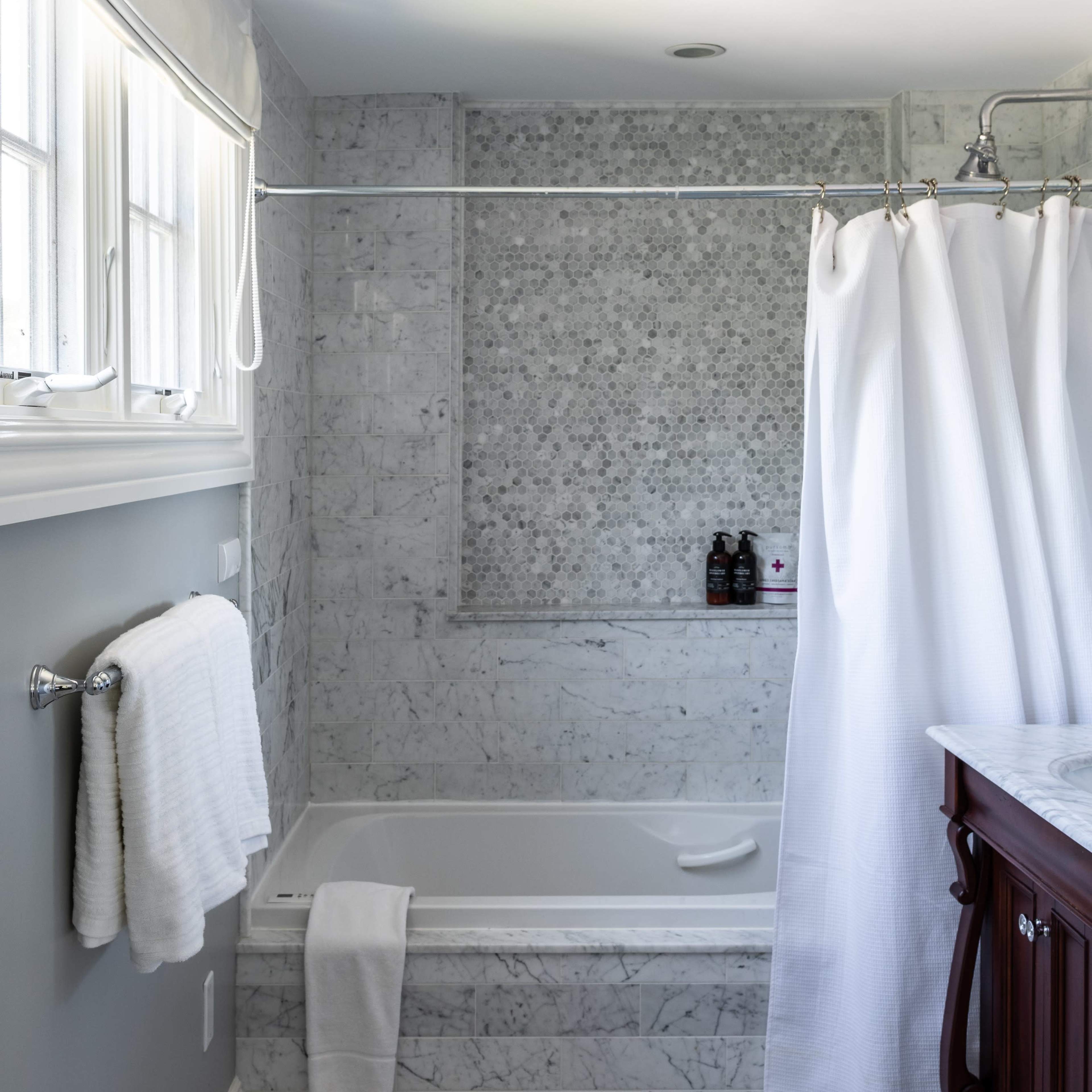 A bathroom with a marble-tiled bathtub, a shower curtain, and a wooden vanity.