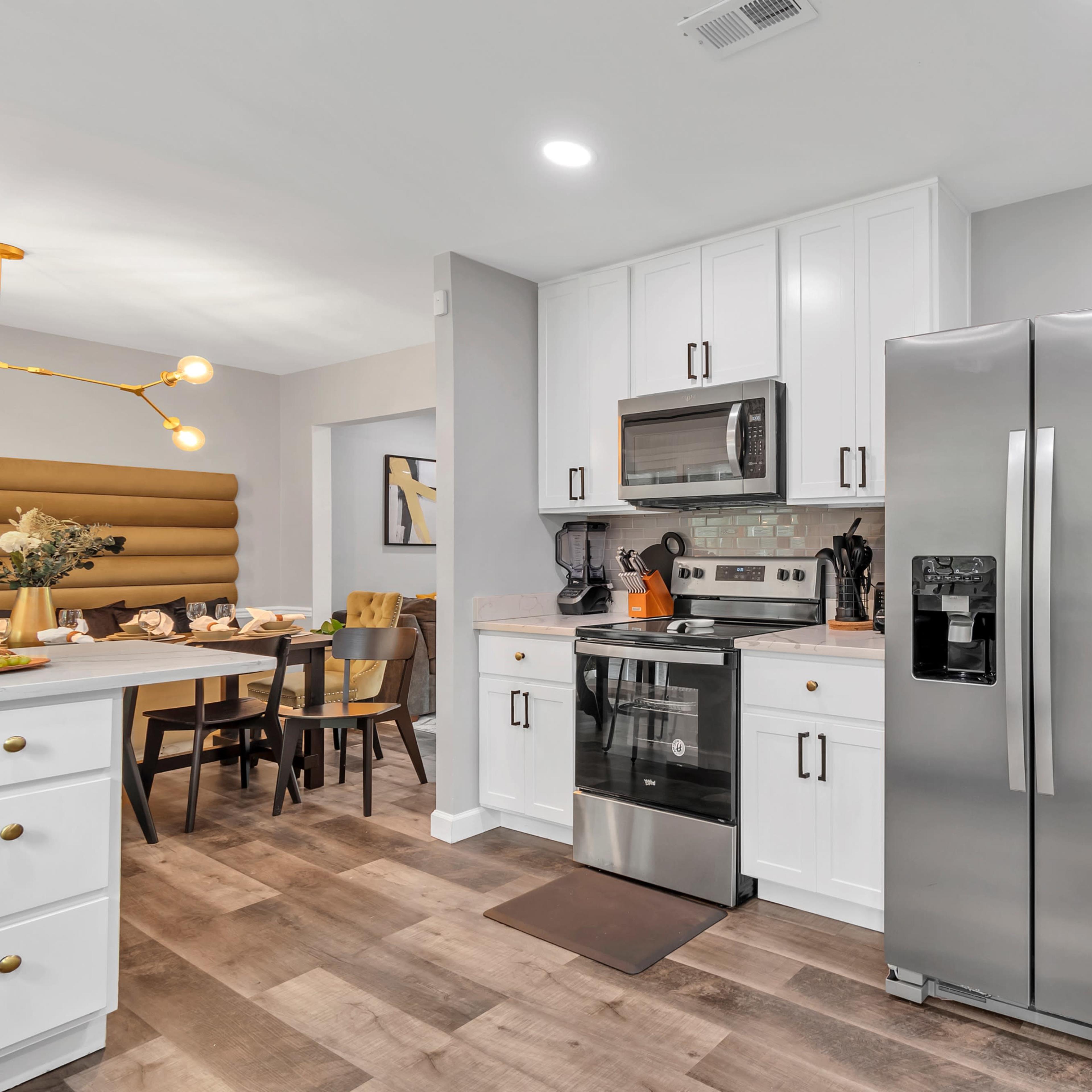 A modern kitchen with white cabinetry, stainless steel appliances, and a dining area featuring a wooden table and chairs.