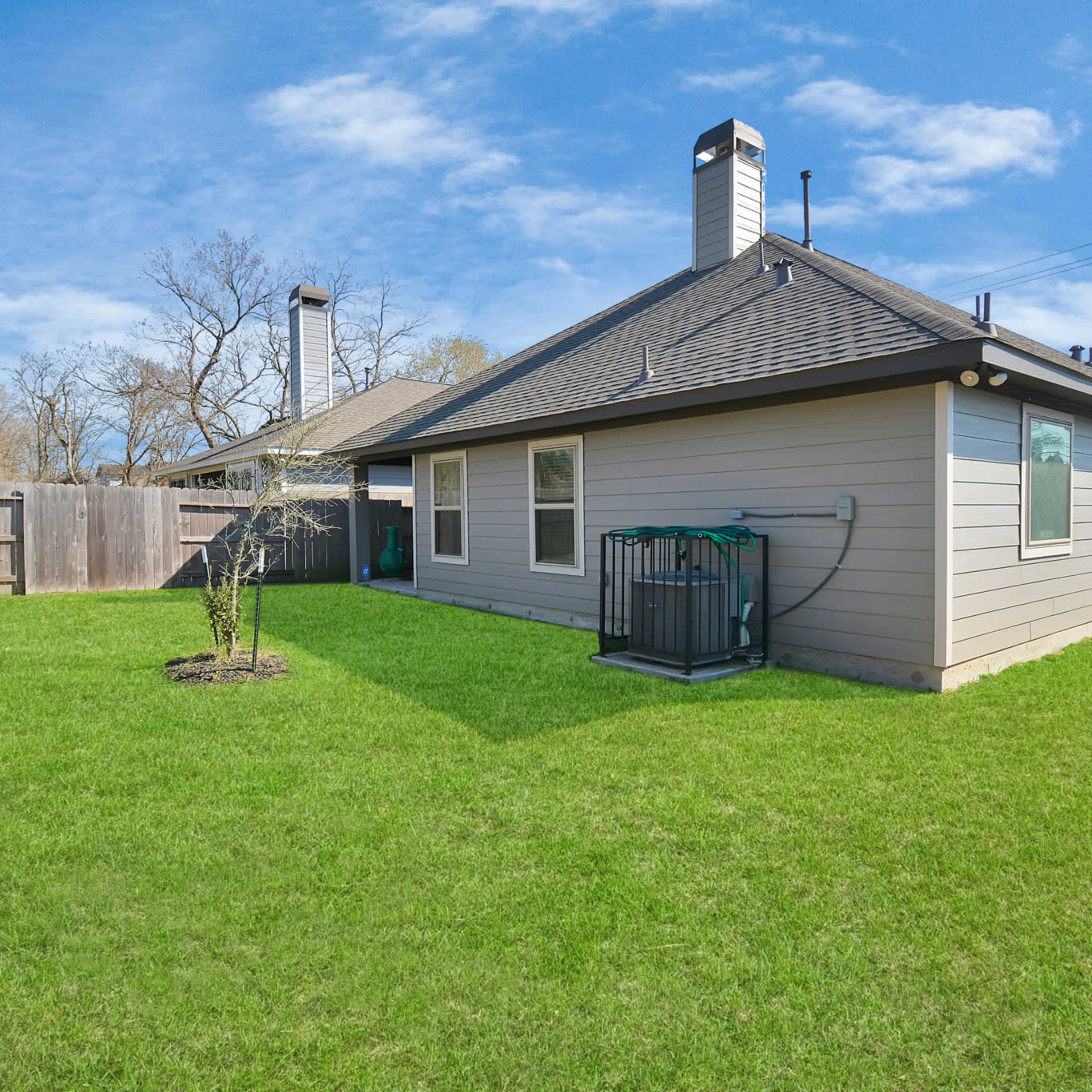 A backyard featuring a well-maintained lawn, a single small tree, and a house with two chimneys and a water connection on one side.
