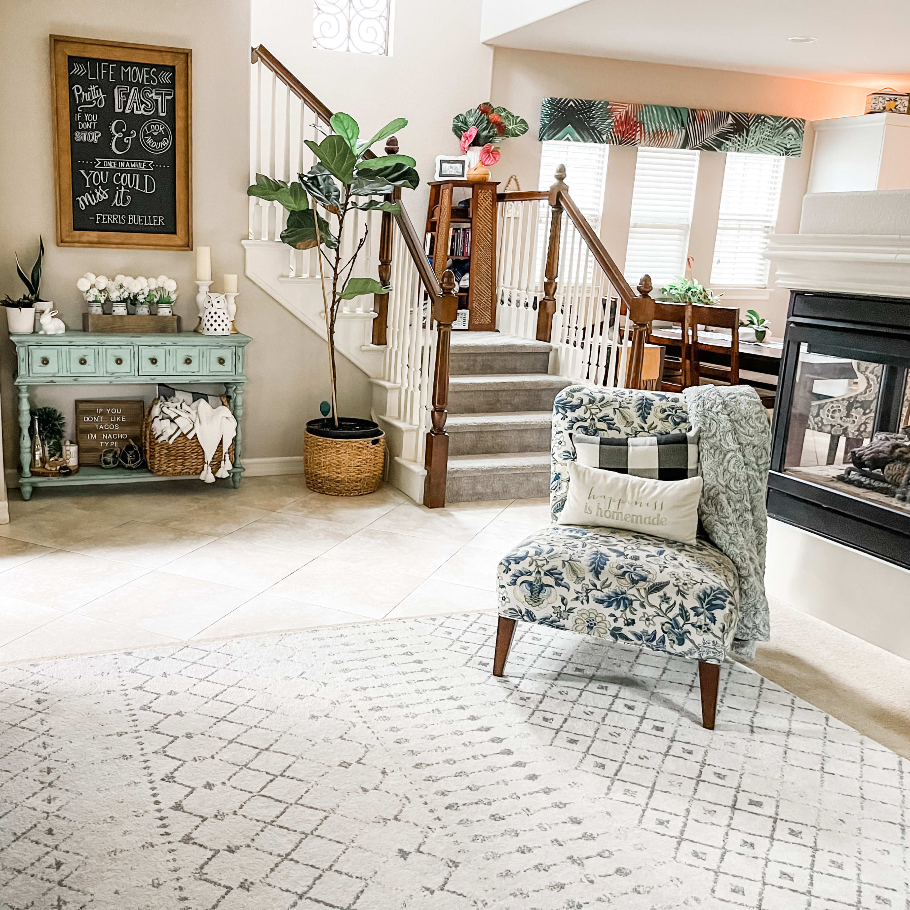 The living room features a light-colored sofa, a patterned armchair, a decorative console table, and a staircase leading to an upper level.