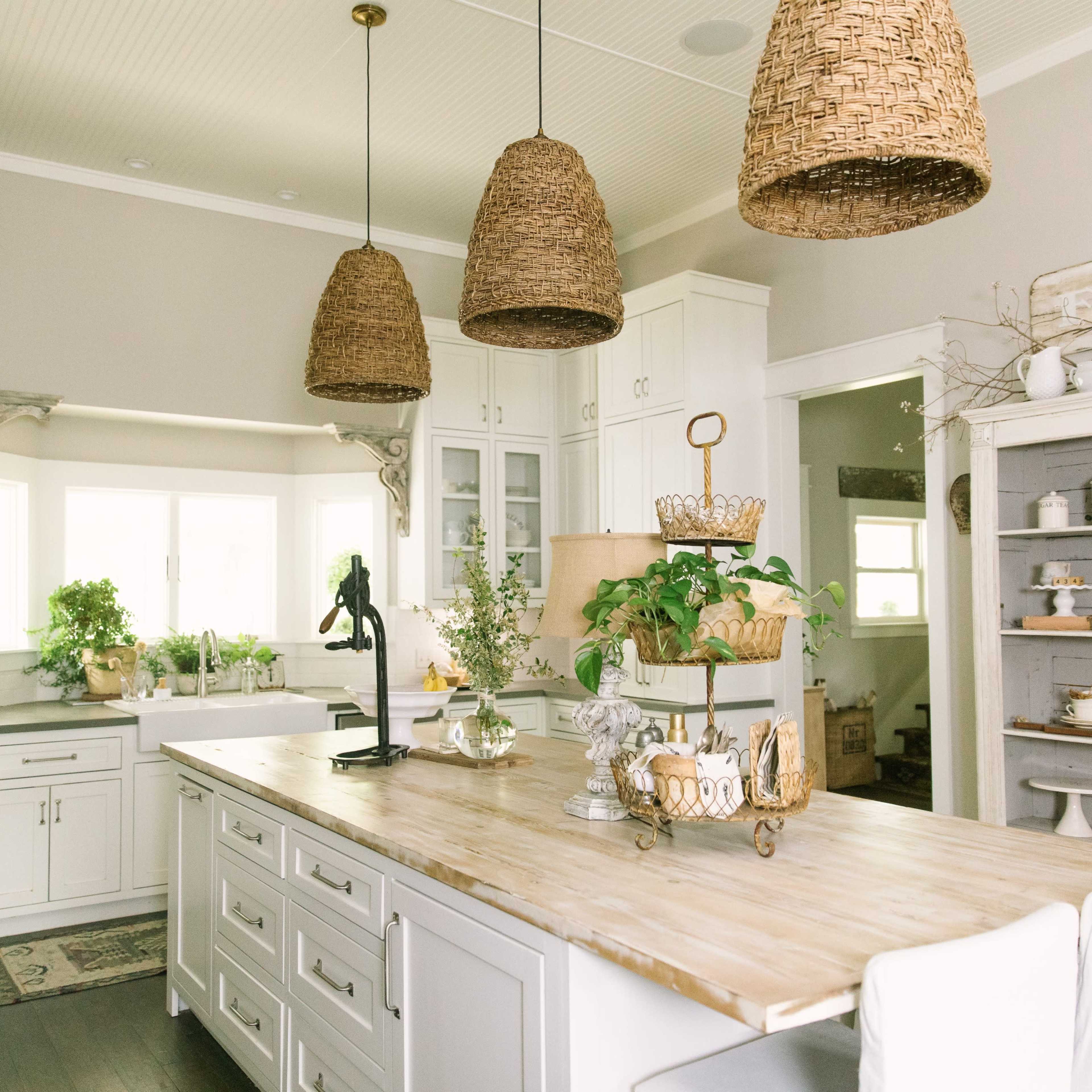 A bright kitchen features a large central island with a wooden countertop, surrounded by white cabinetry and hanging woven light fixtures.
