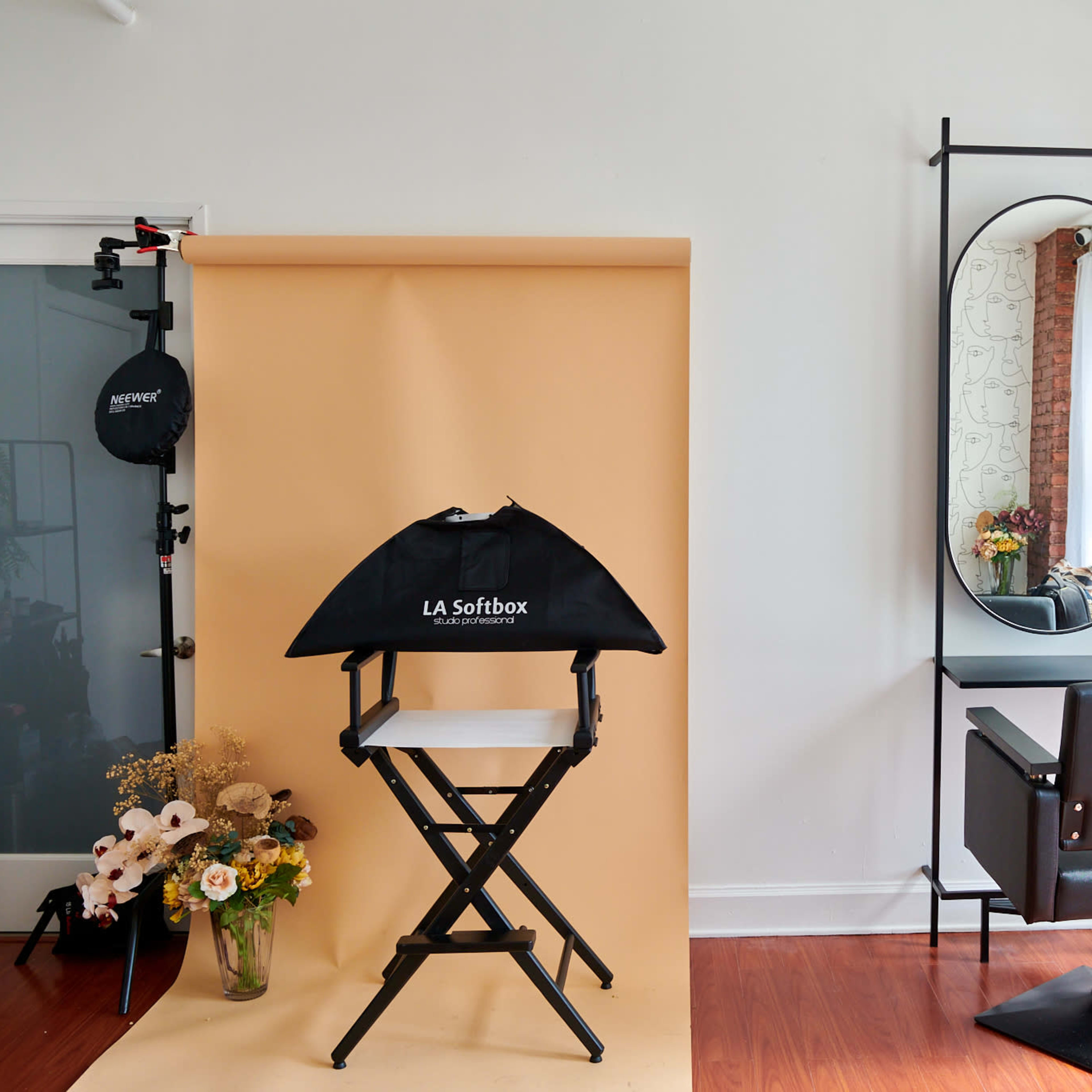 The scene shows a bright, minimalist hair salon with a folding director's chair, a makeup mirror, and a shelf displaying beauty products against a backdrop of warm, neutral tones.