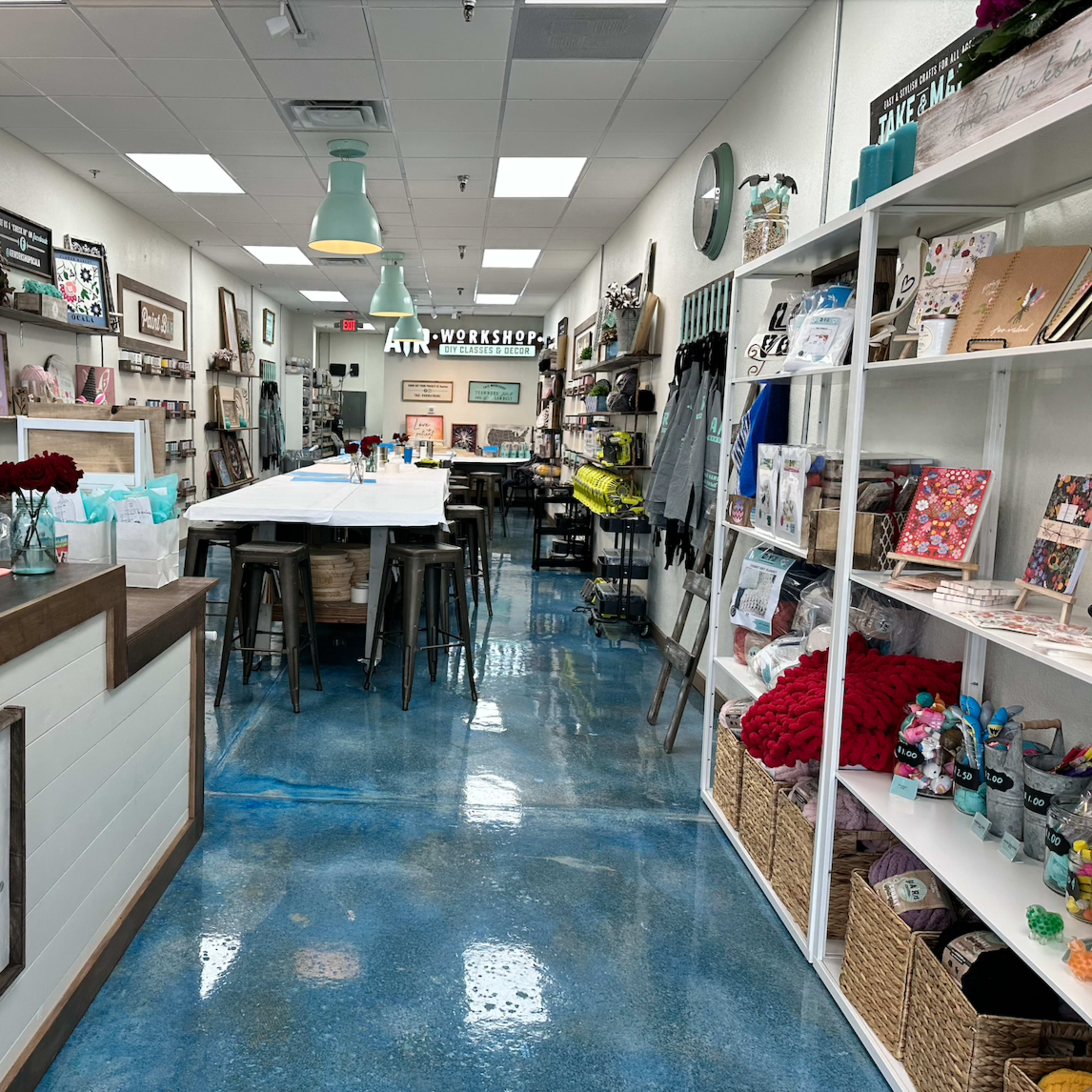 The interior of a crafting store with a long table in the center, surrounded by shelves displaying various art supplies and finished projects.