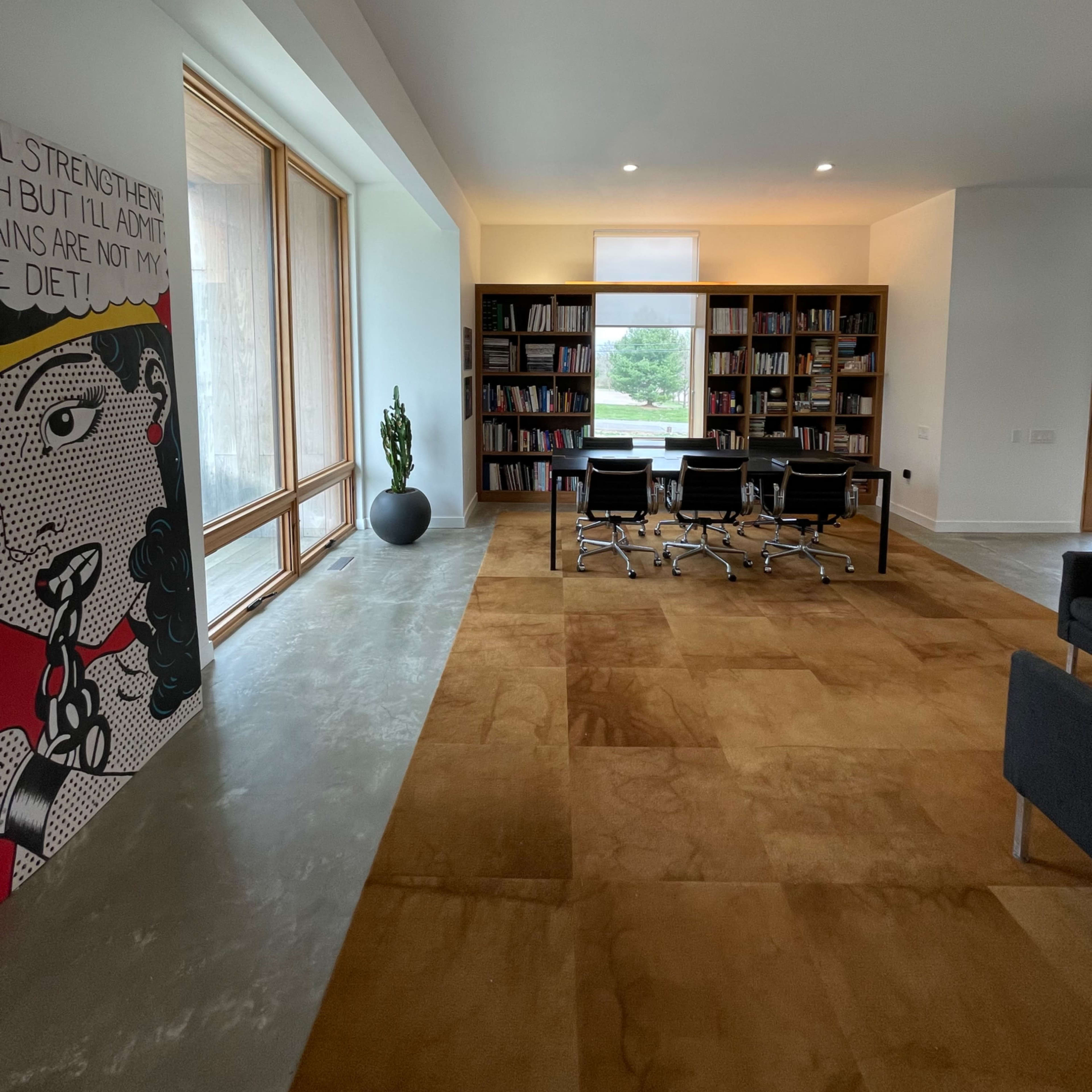 A modern office space with a bookshelf, a meeting area featuring four chairs, and large windows allowing natural light.