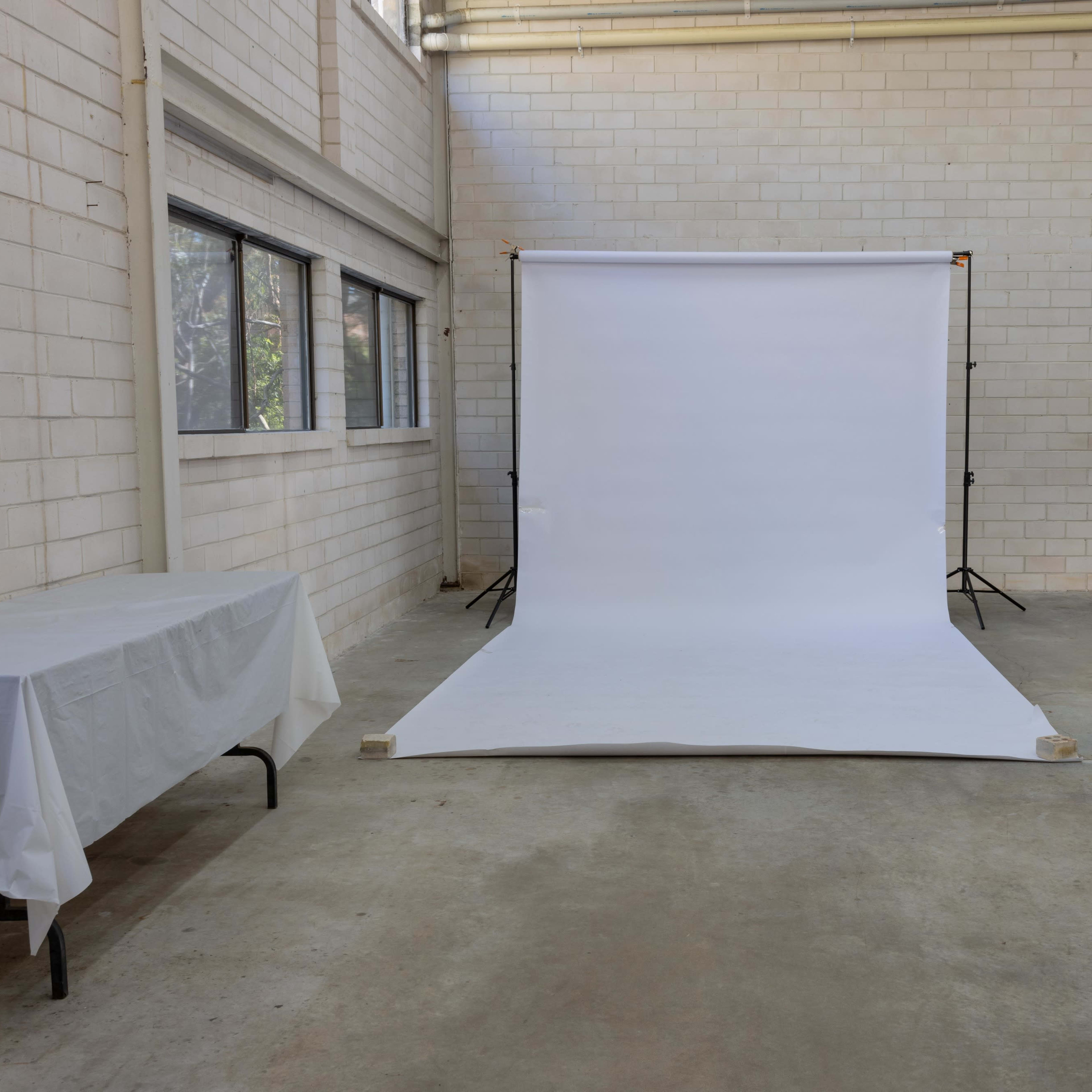An empty studio space features a white backdrop on the floor, illuminated by natural light from large windows.