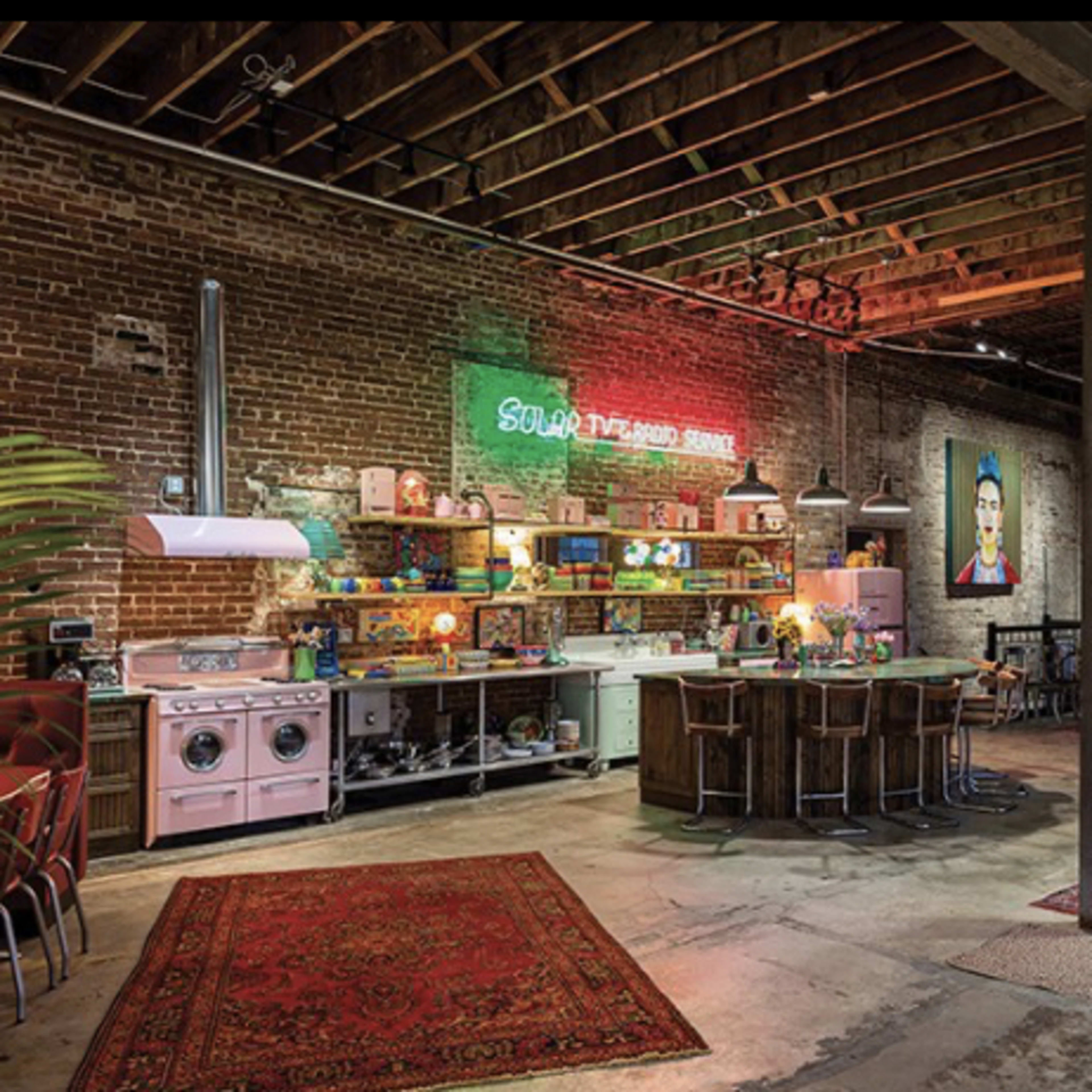 A spacious industrial-style kitchen and living area with exposed brick walls, wooden beams, and a mix of colorful furnishings.