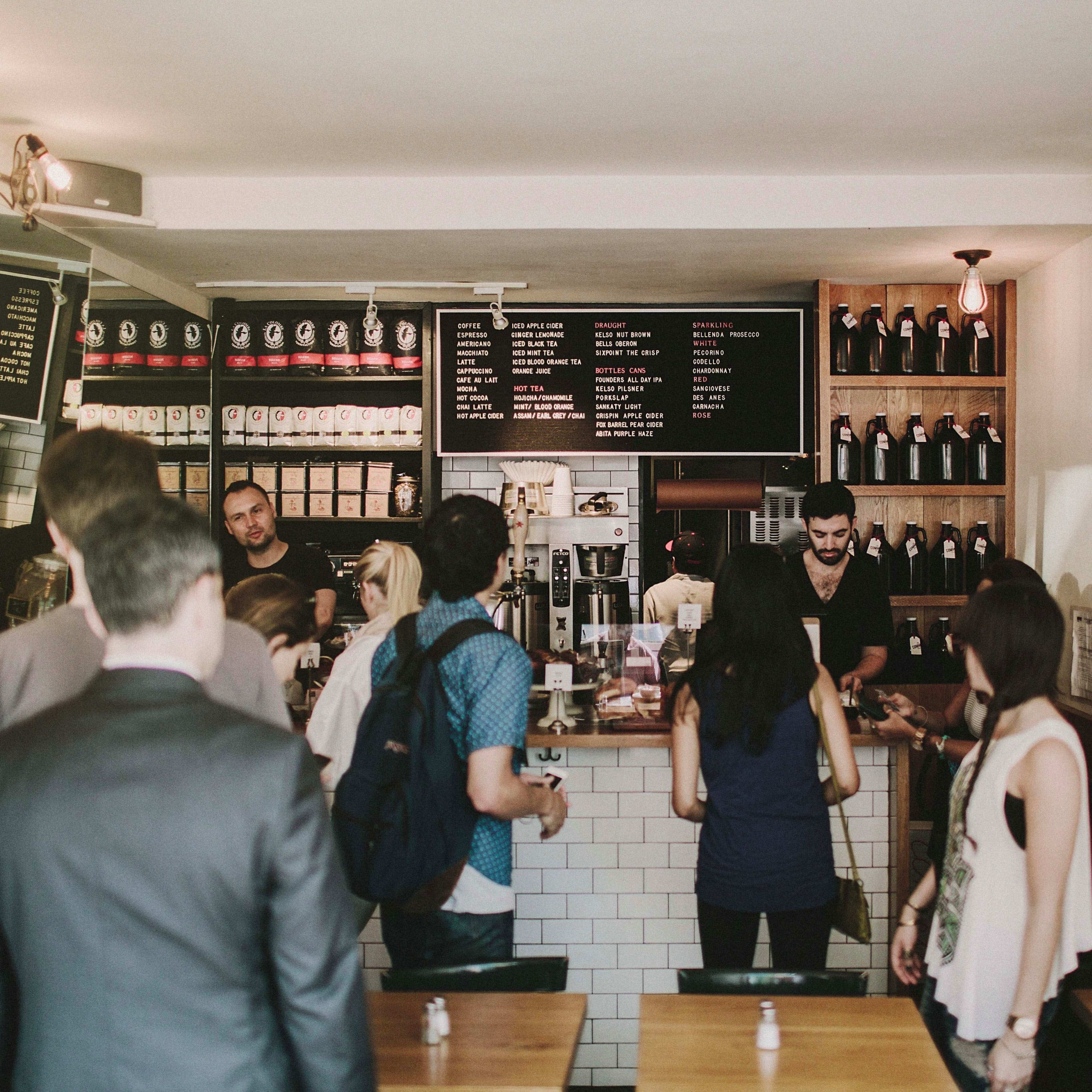 A group of customers engages with staff at a coffee shop counter while others wait in line.