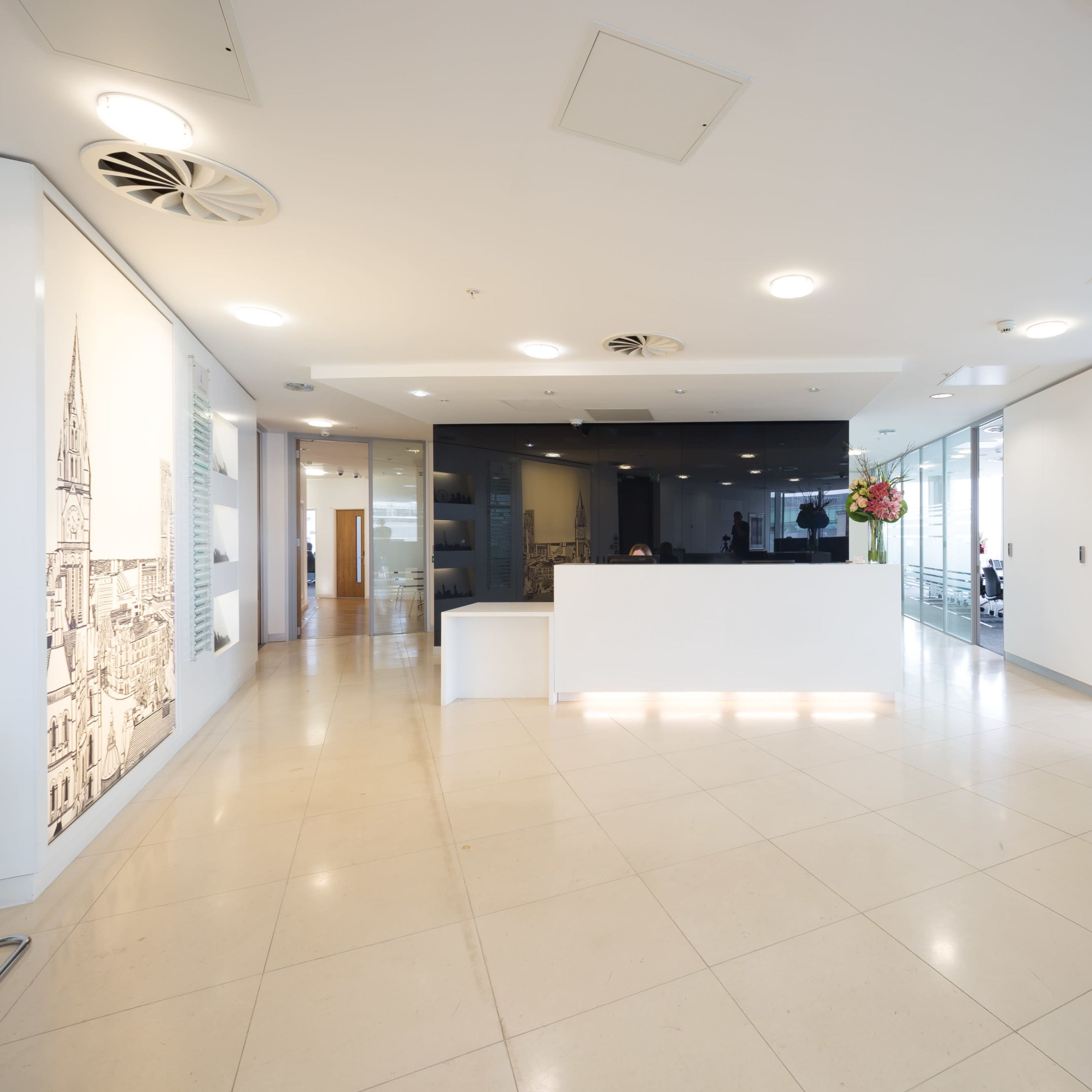 A modern office reception area with a sleek white desk, glass partitions, and a minimalist seating arrangement.