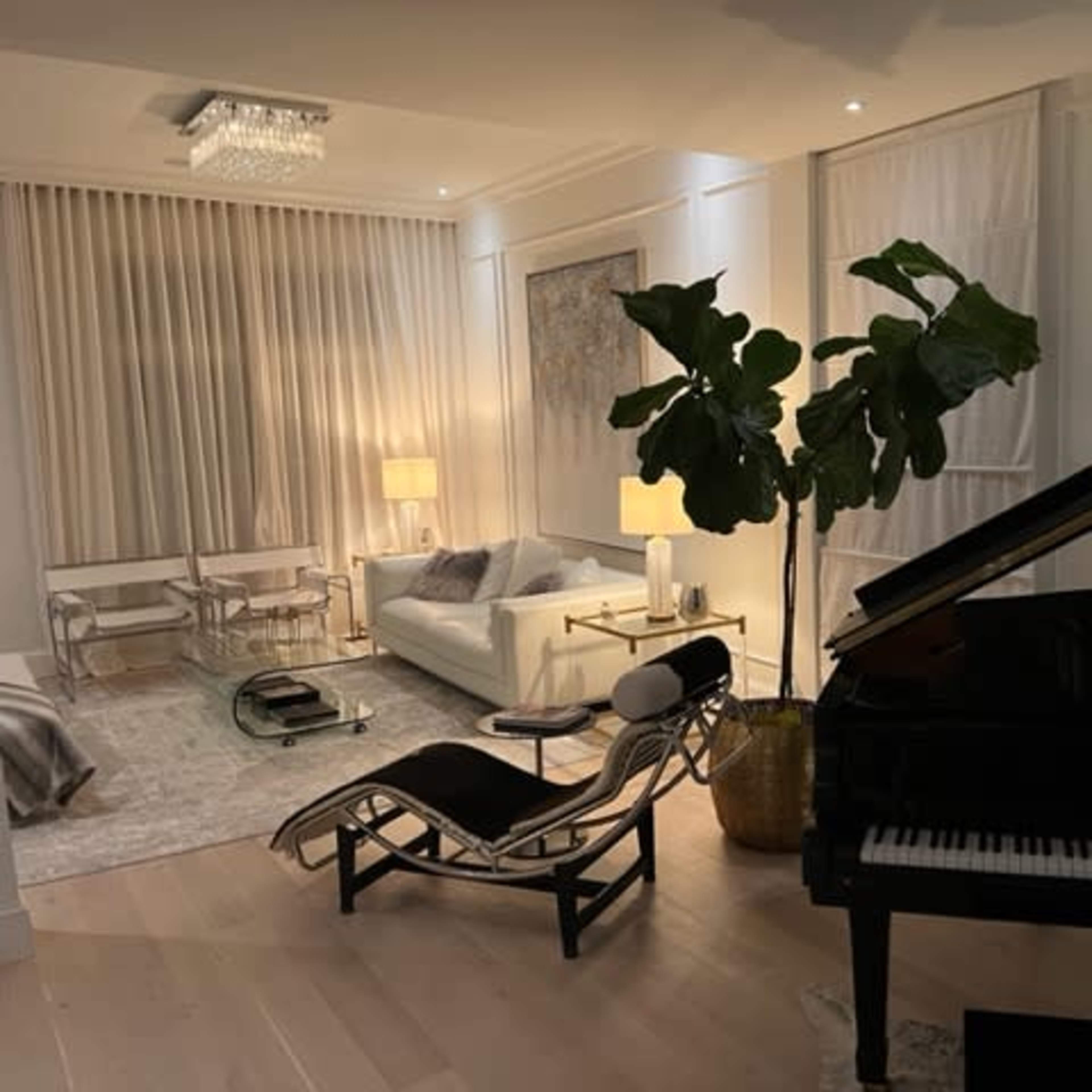 A modern living room featuring a grand piano, a white sofa, a decorative plant, a glass dining table, and abstract art on the walls.