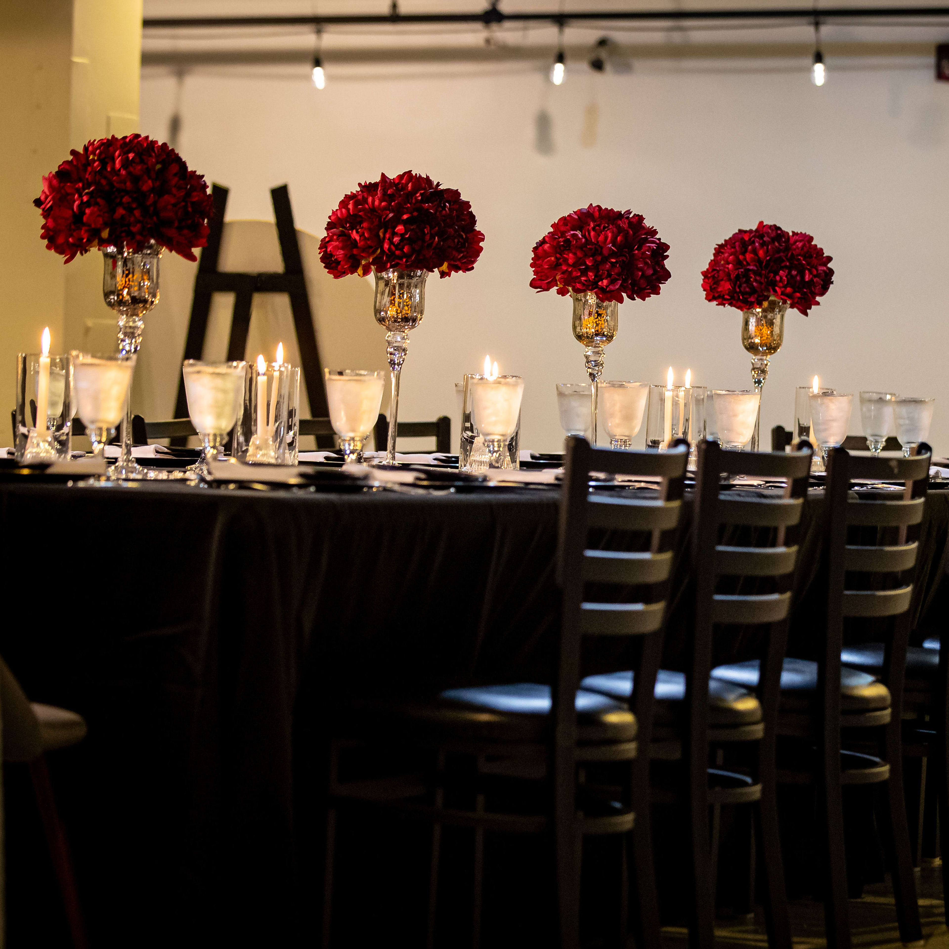 A long dining table is set with elegant glassware, floral arrangements, and candles, surrounded by black chairs.