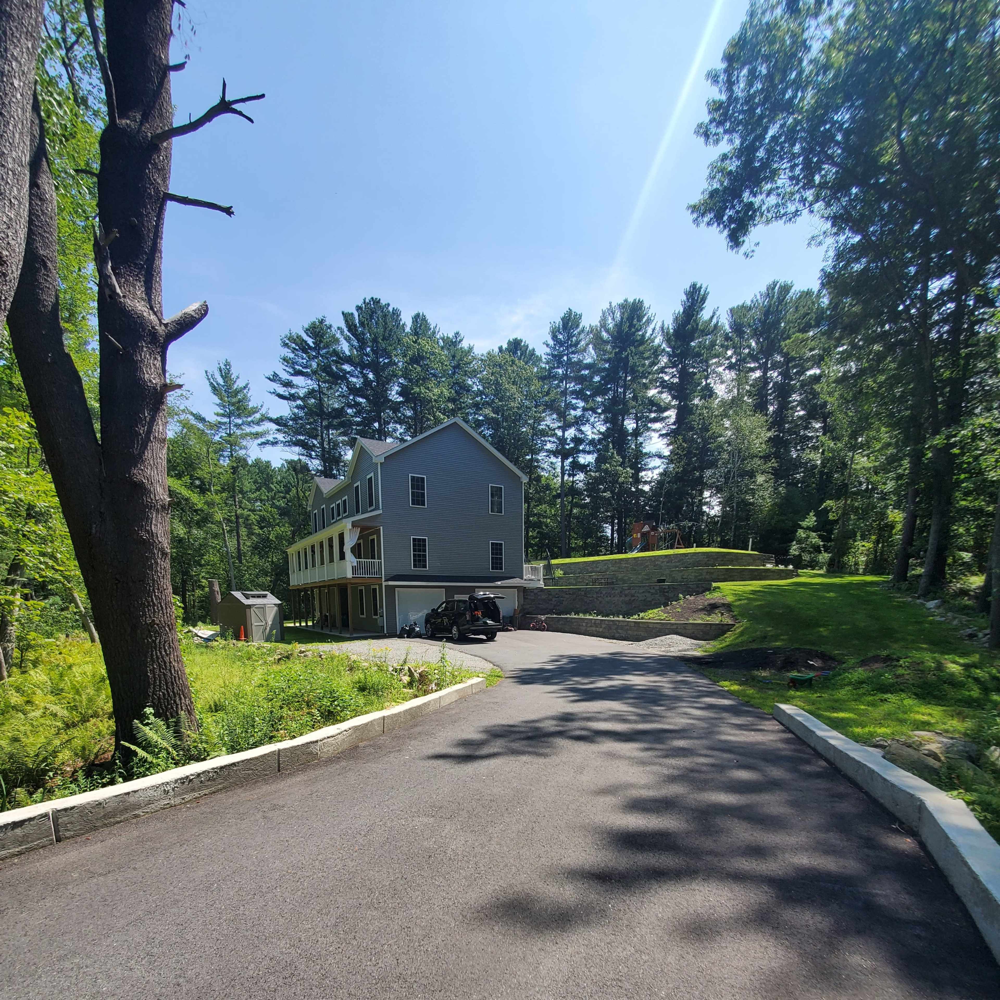 A paved driveway leads up to a gray house surrounded by trees.