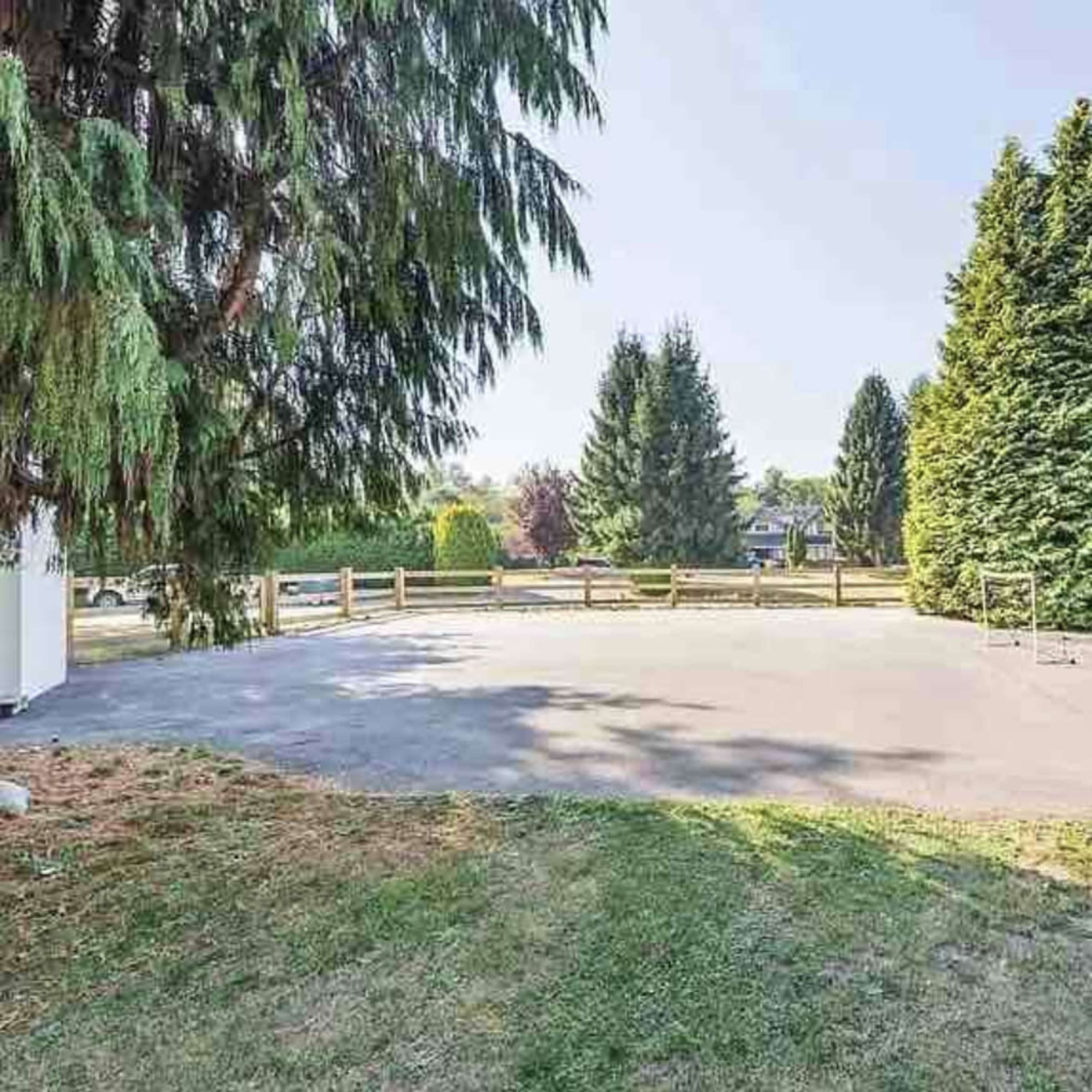 An open, paved area surrounded by tall green trees and a wooden fence.