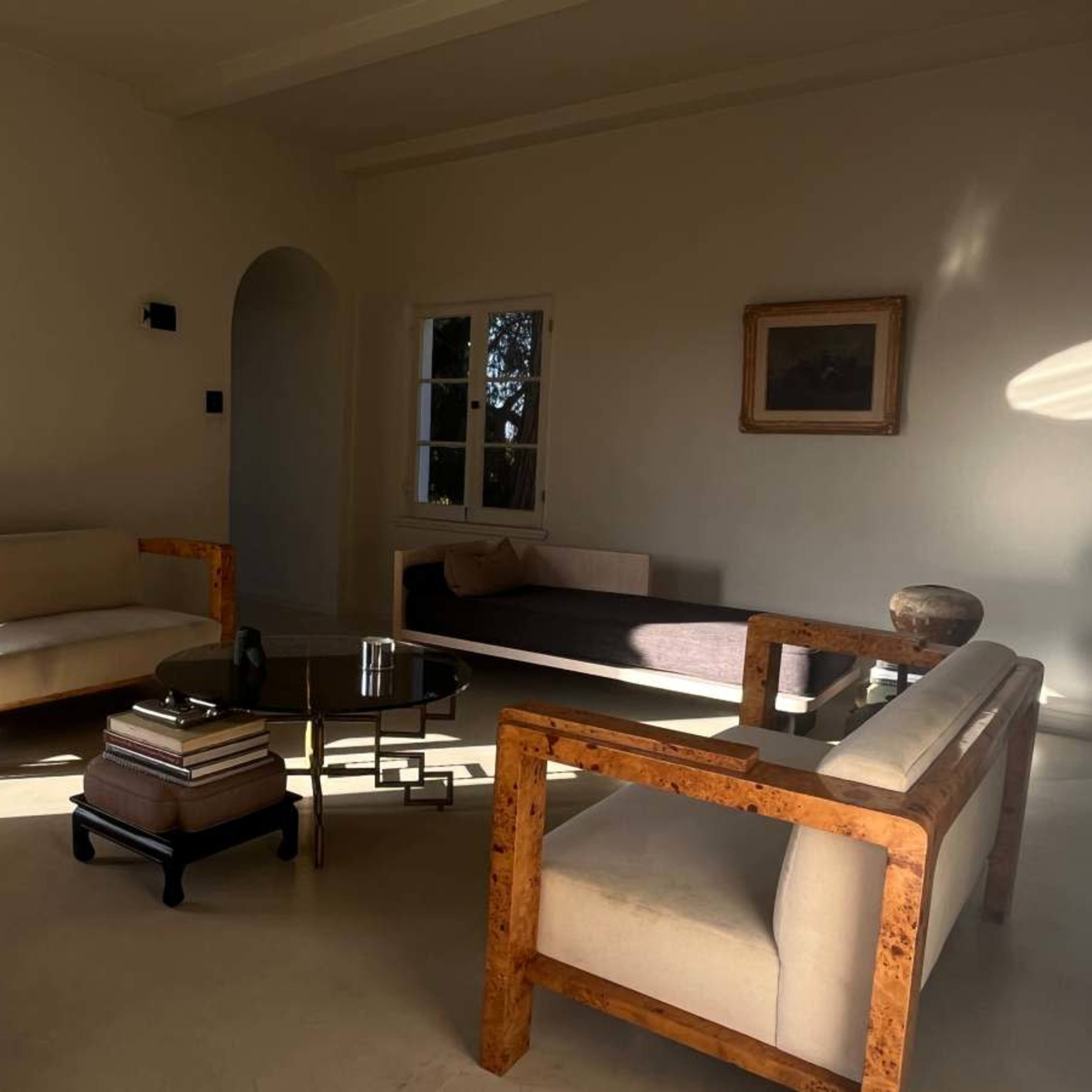 A minimalist living room with two sofas, a coffee table stacked with books, and a window letting in natural light.