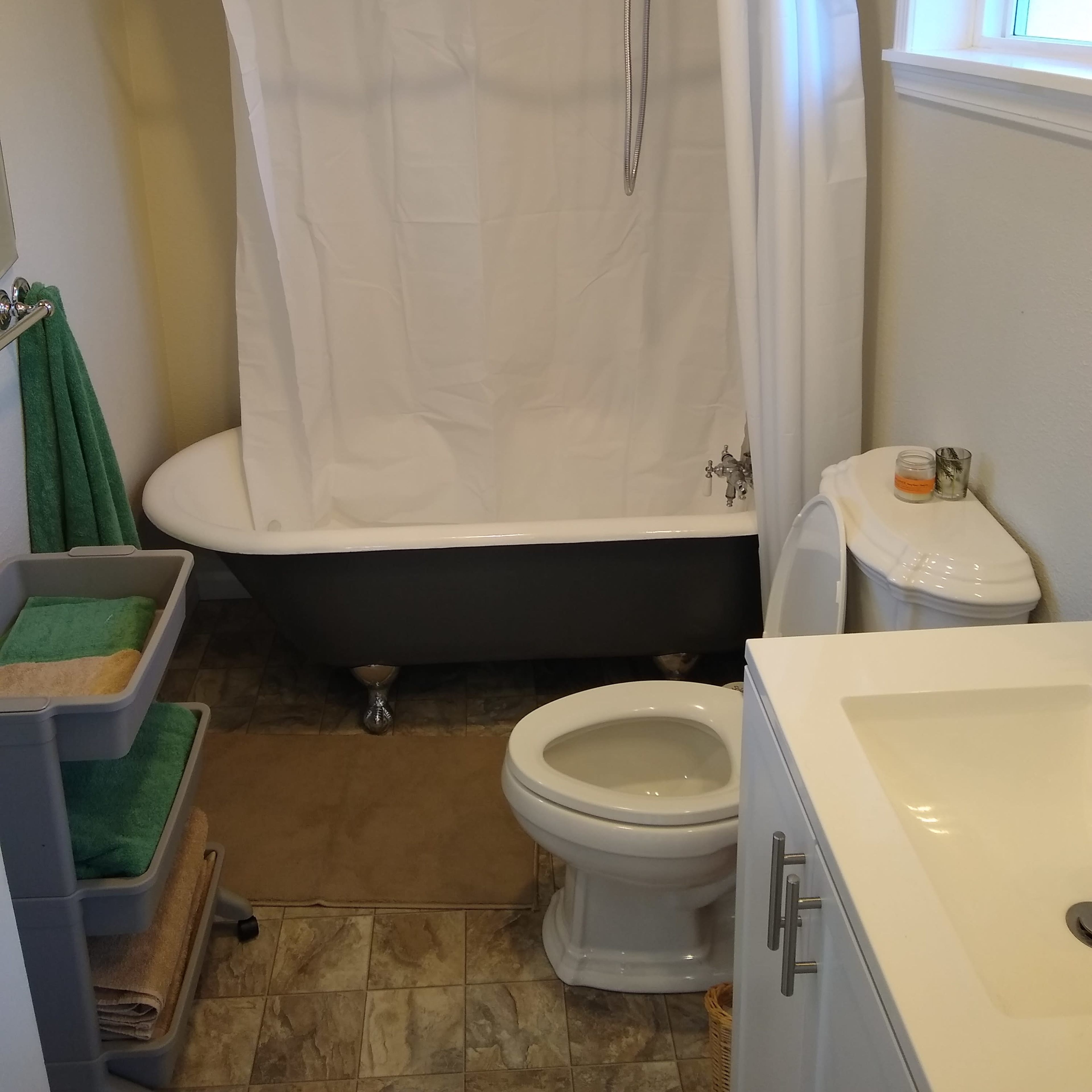 A small bathroom containing a clawfoot bathtub with a shower curtain, a toilet, and a vanity with a sink.