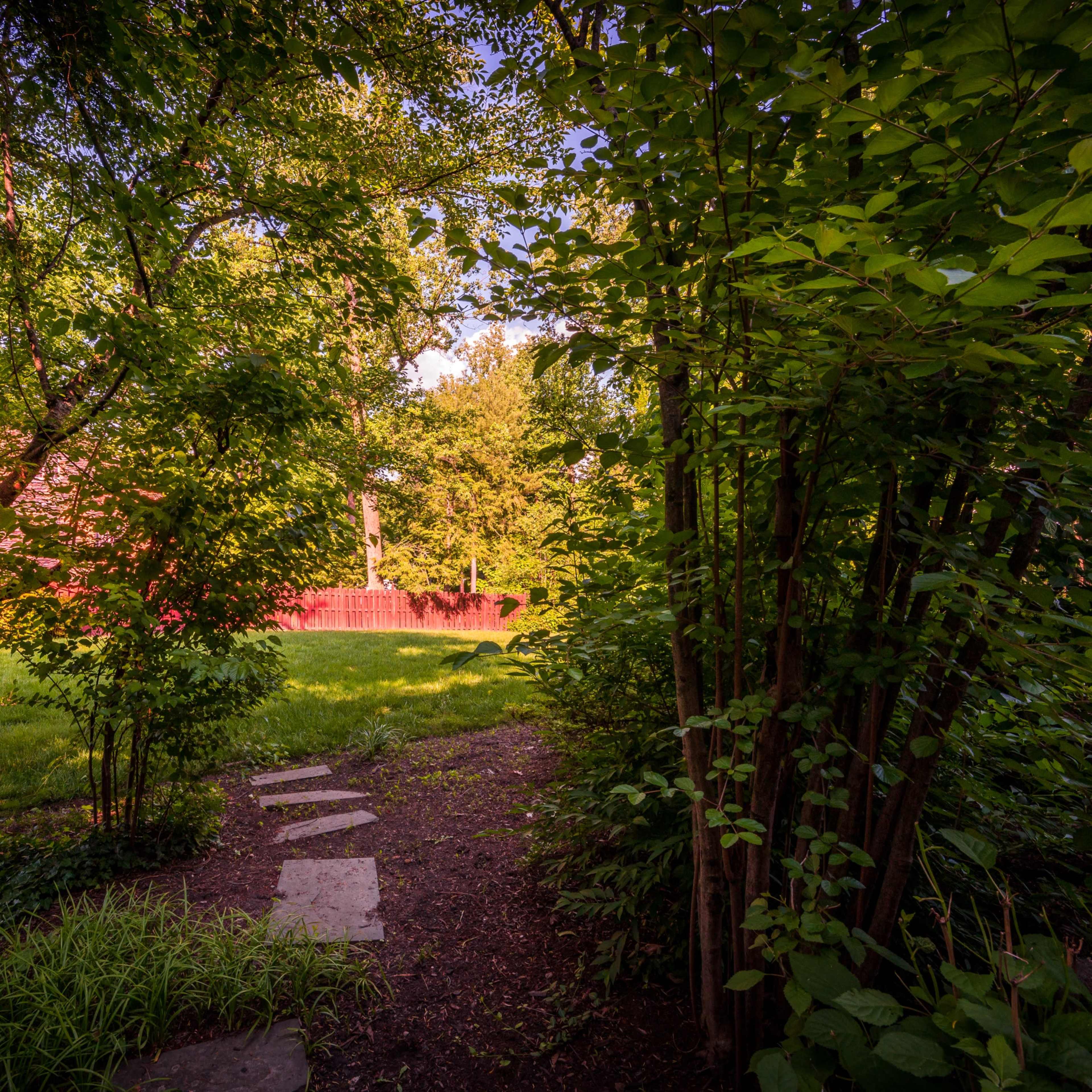 A stone pathway leads through a green garden surrounded by trees and bushes.