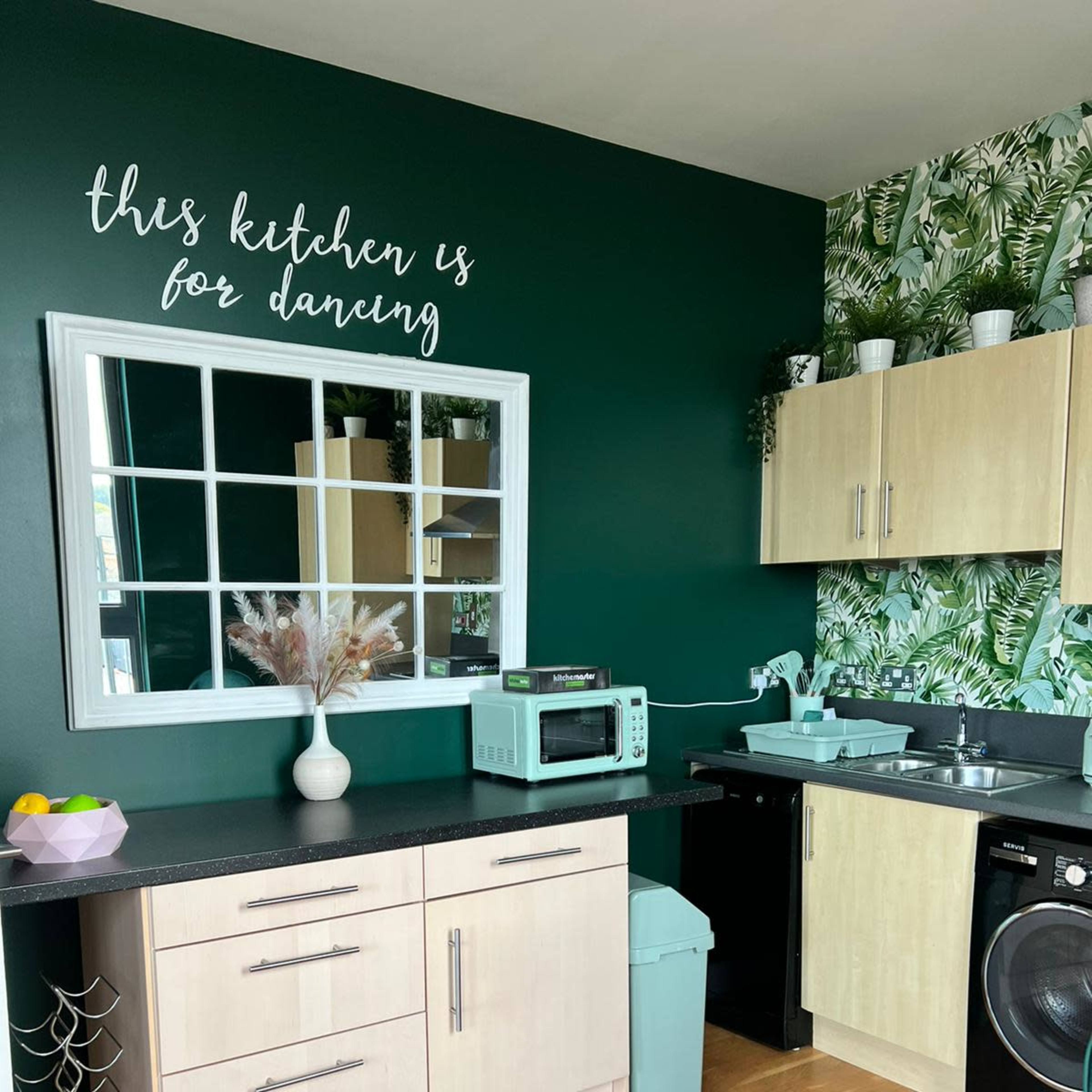 A kitchen featuring a dark green accent wall, a large mirror, modern cabinetry, and tropical-themed wallpaper.