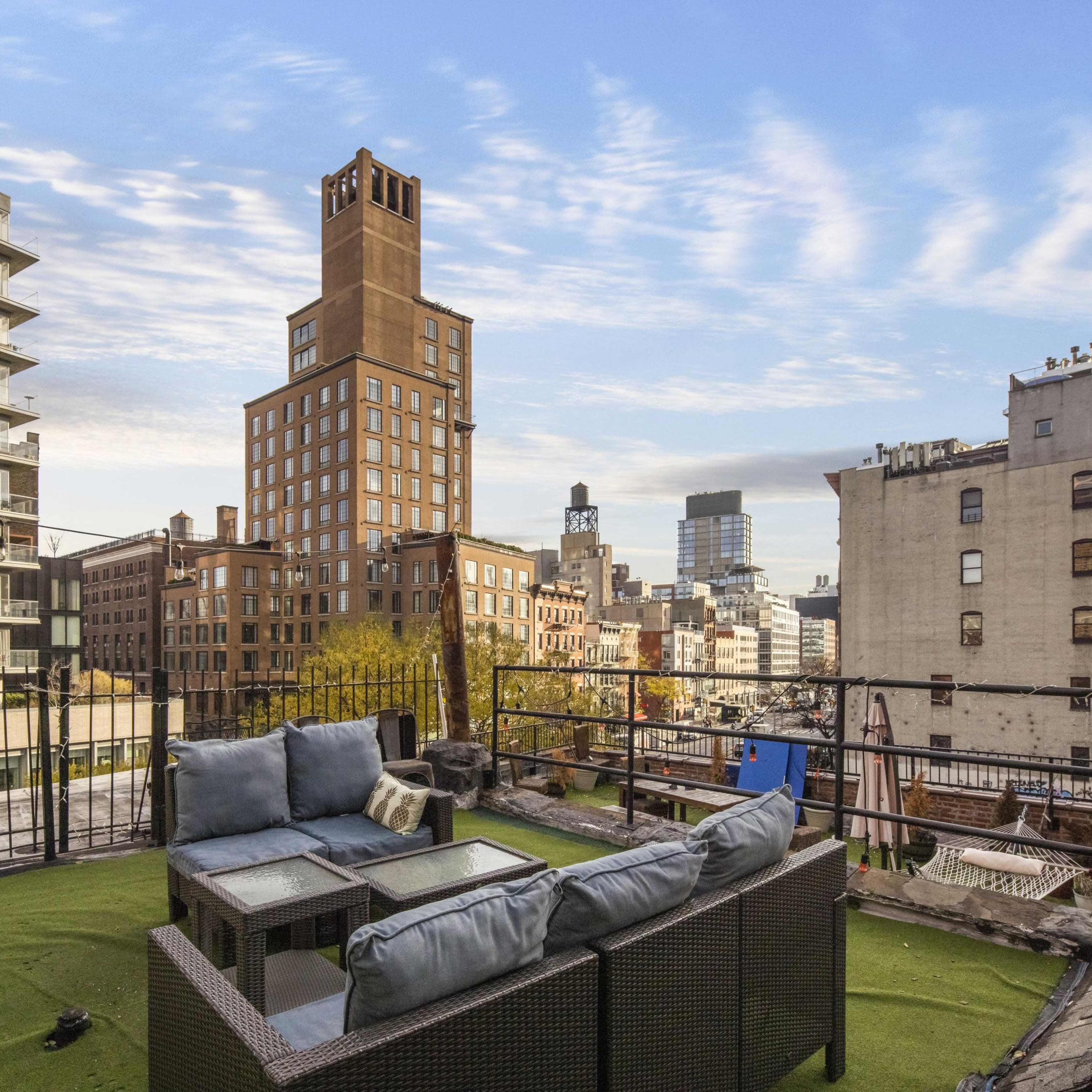 A rooftop terrace features a seating area with a view of city buildings and a cloudy sky in the background.