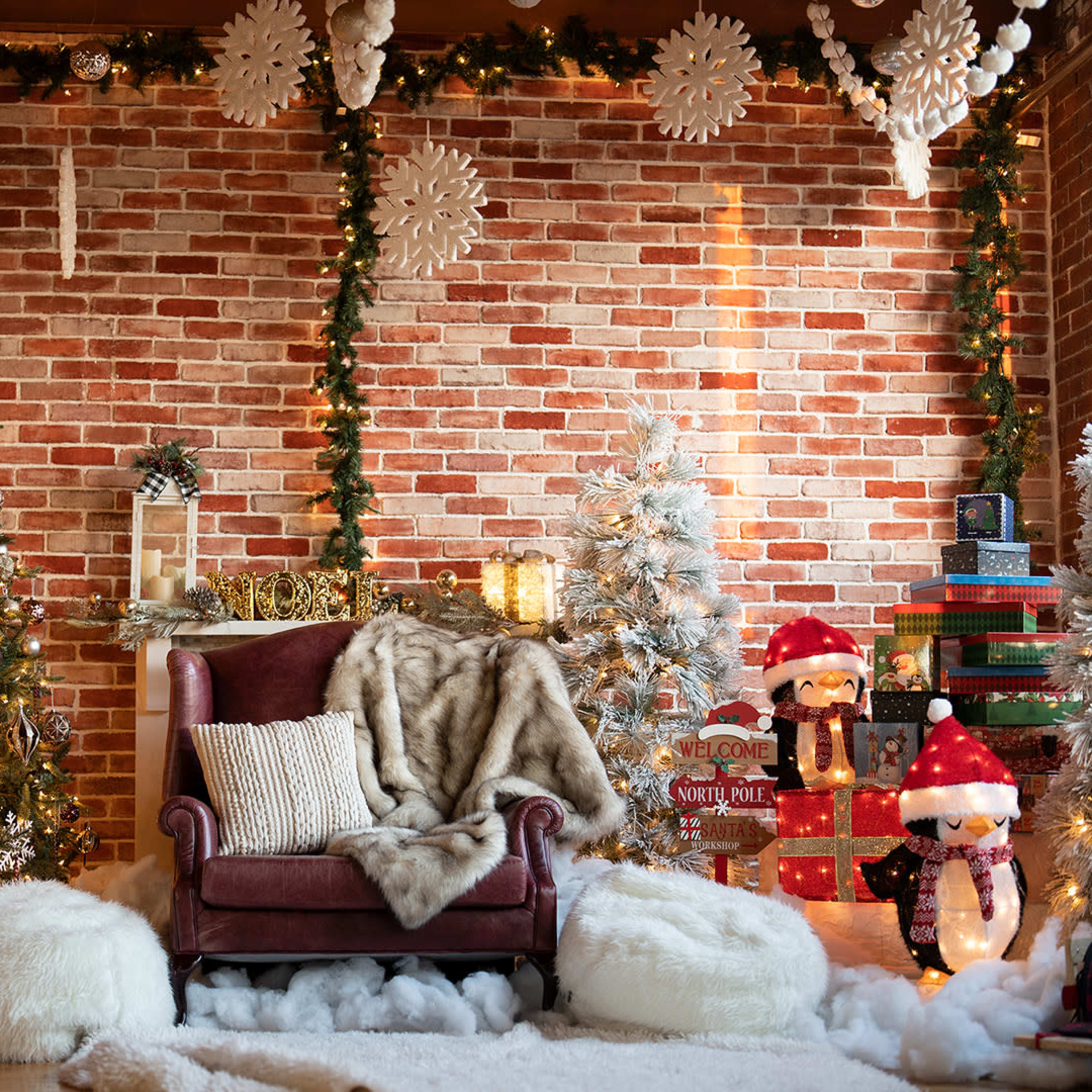 A cozy holiday setting with a plush chair, decorated Christmas trees, and festive ornaments against a brick wall.