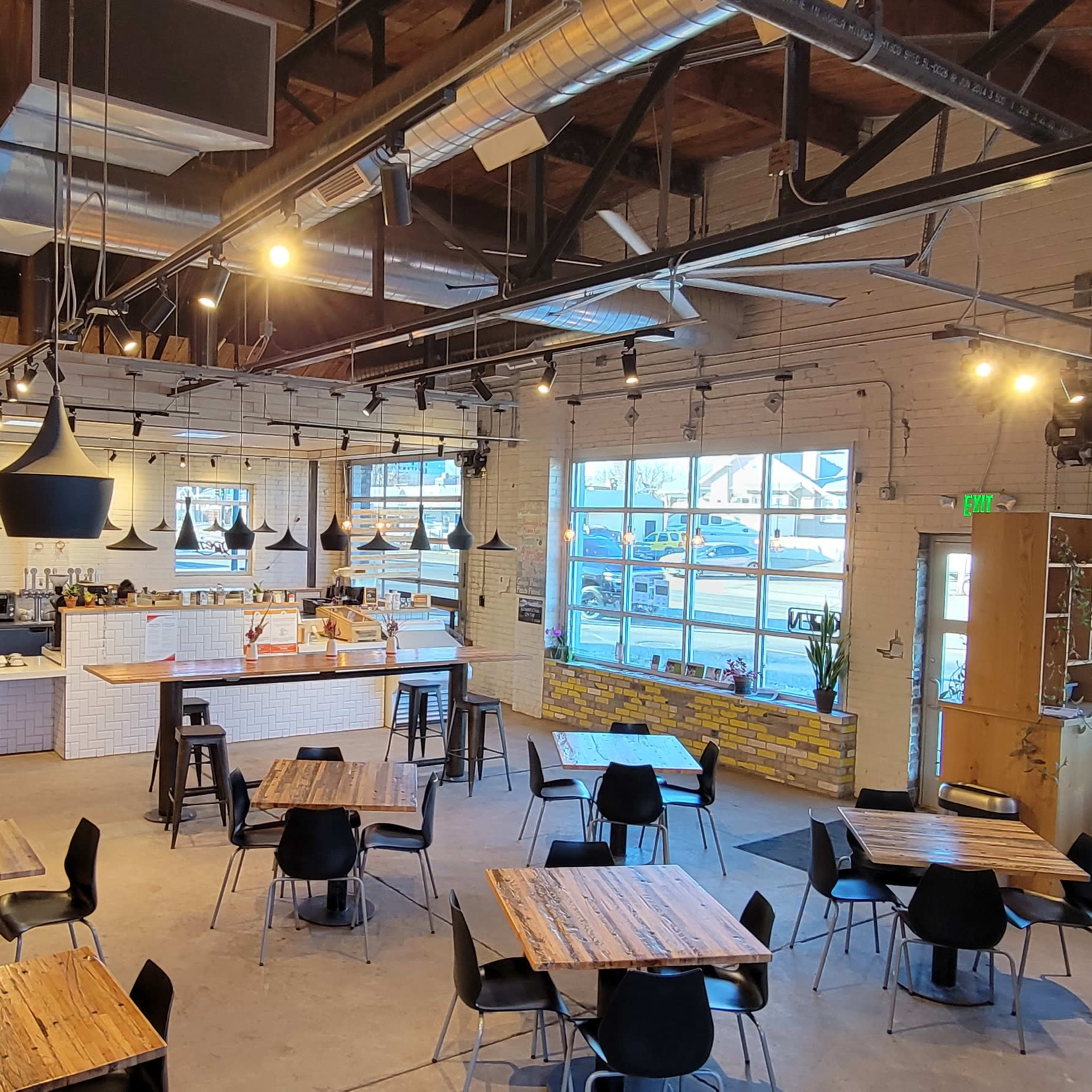 A spacious cafe with black chairs and wooden tables, featuring a large counter behind which baristas work.