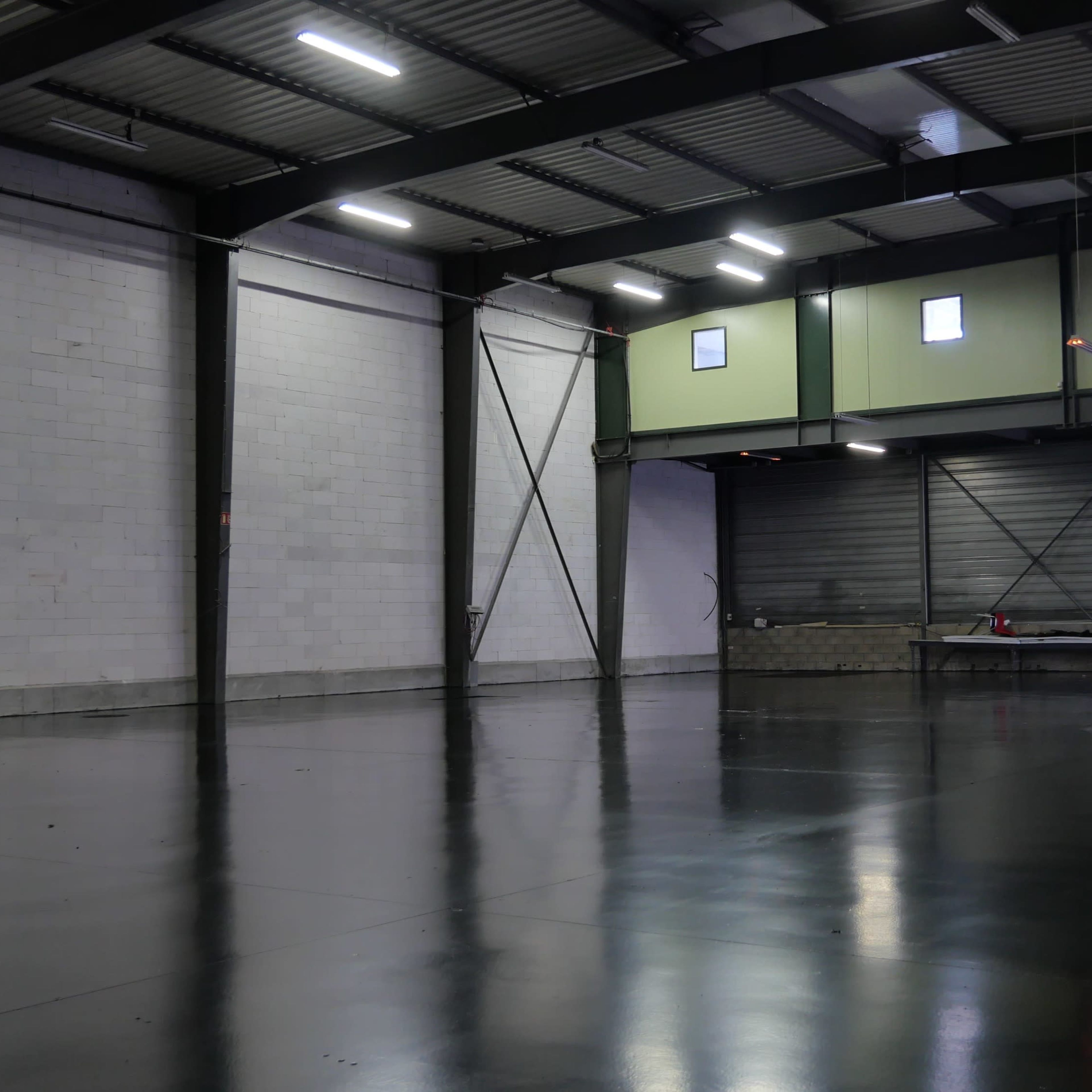 A spacious, industrial-style warehouse with polished concrete floors and white, gray, and green walls.