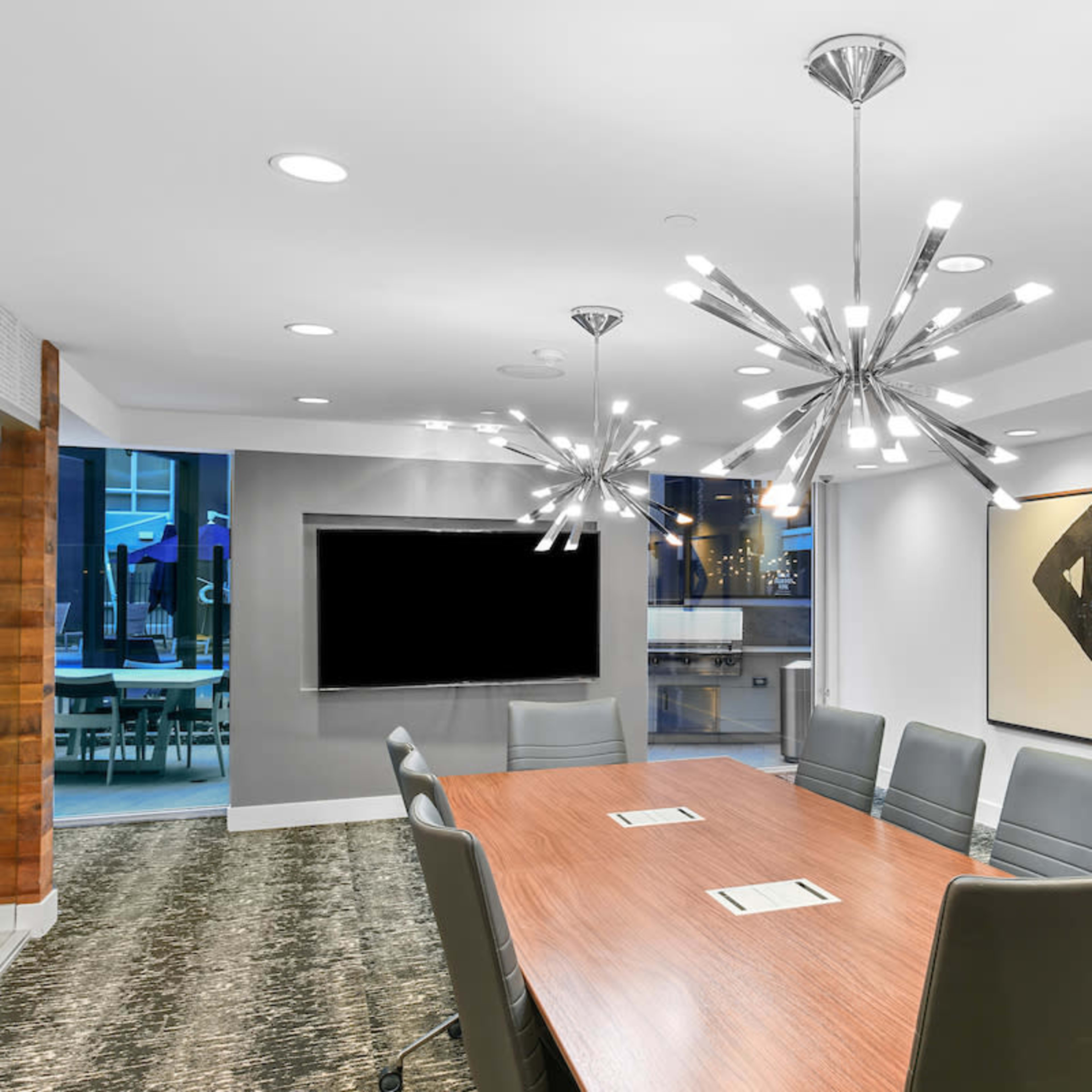 A modern conference room features a long wooden table surrounded by ergonomic chairs, with two contemporary light fixtures and large abstract artworks on the walls.