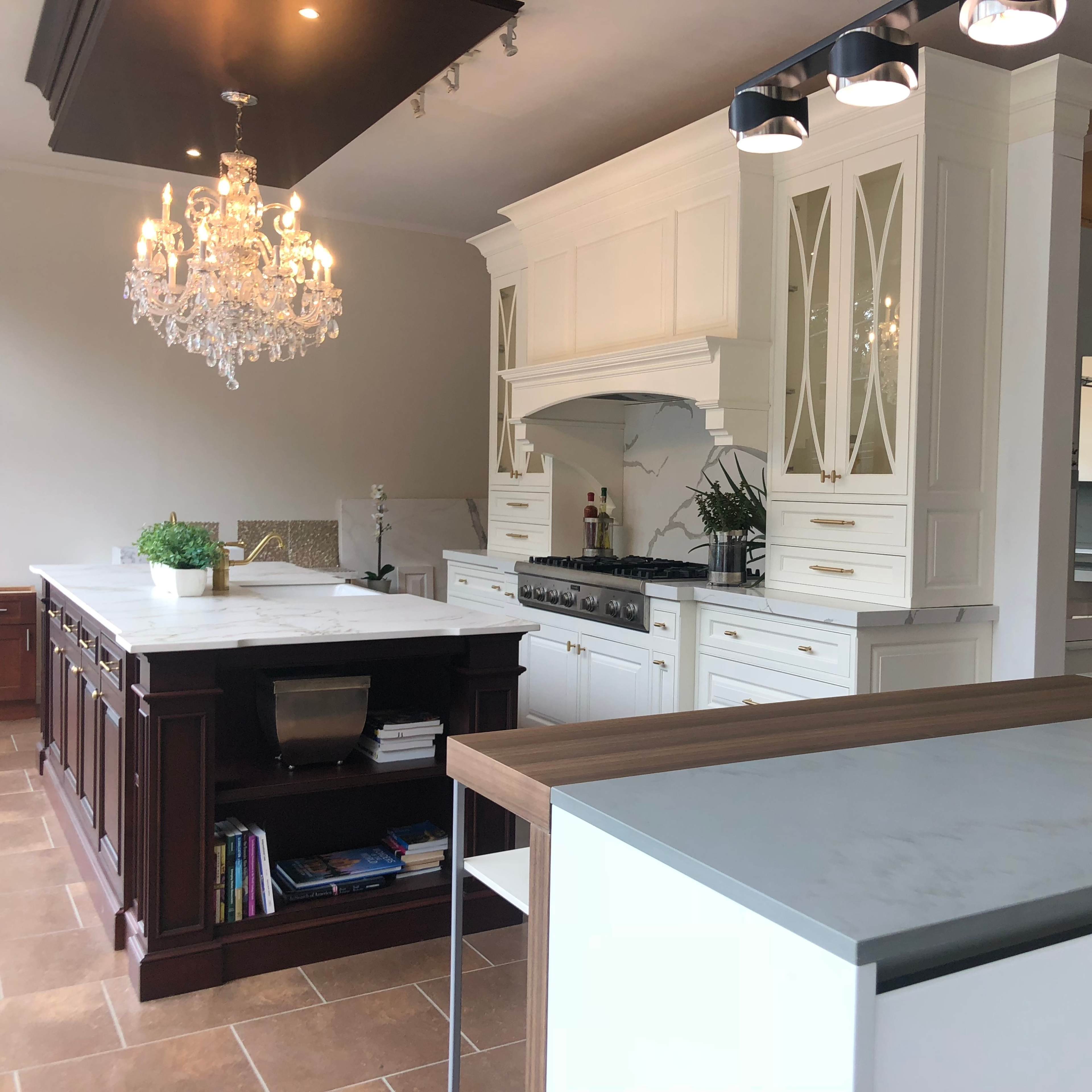 A modern kitchen featuring white cabinetry, a large central island with a wooden and marble counter, and a chandelier overhead.