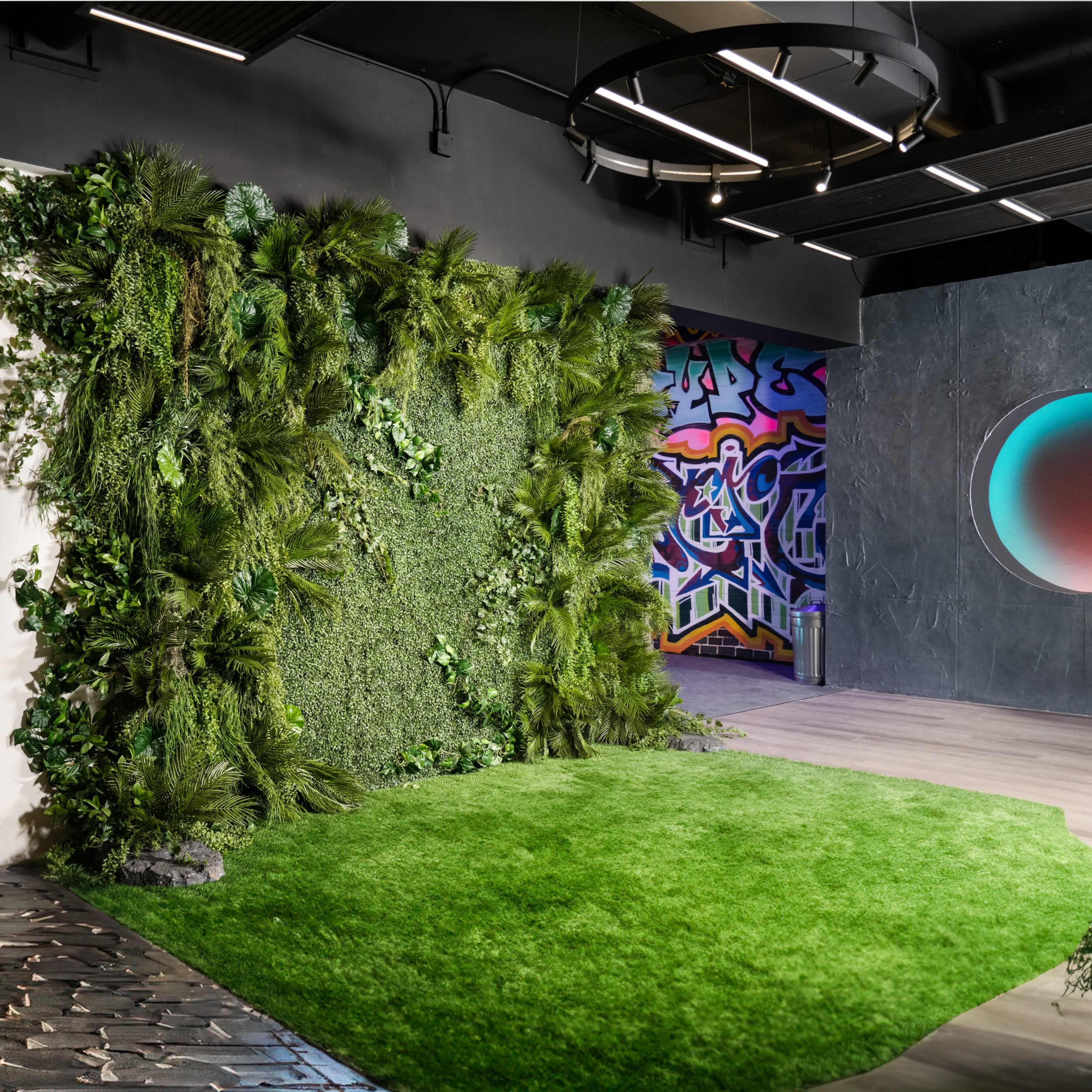 The interior features a living wall of greenery beside a mural with vibrant graffiti, set against a modern design of open spaces and varied textures.