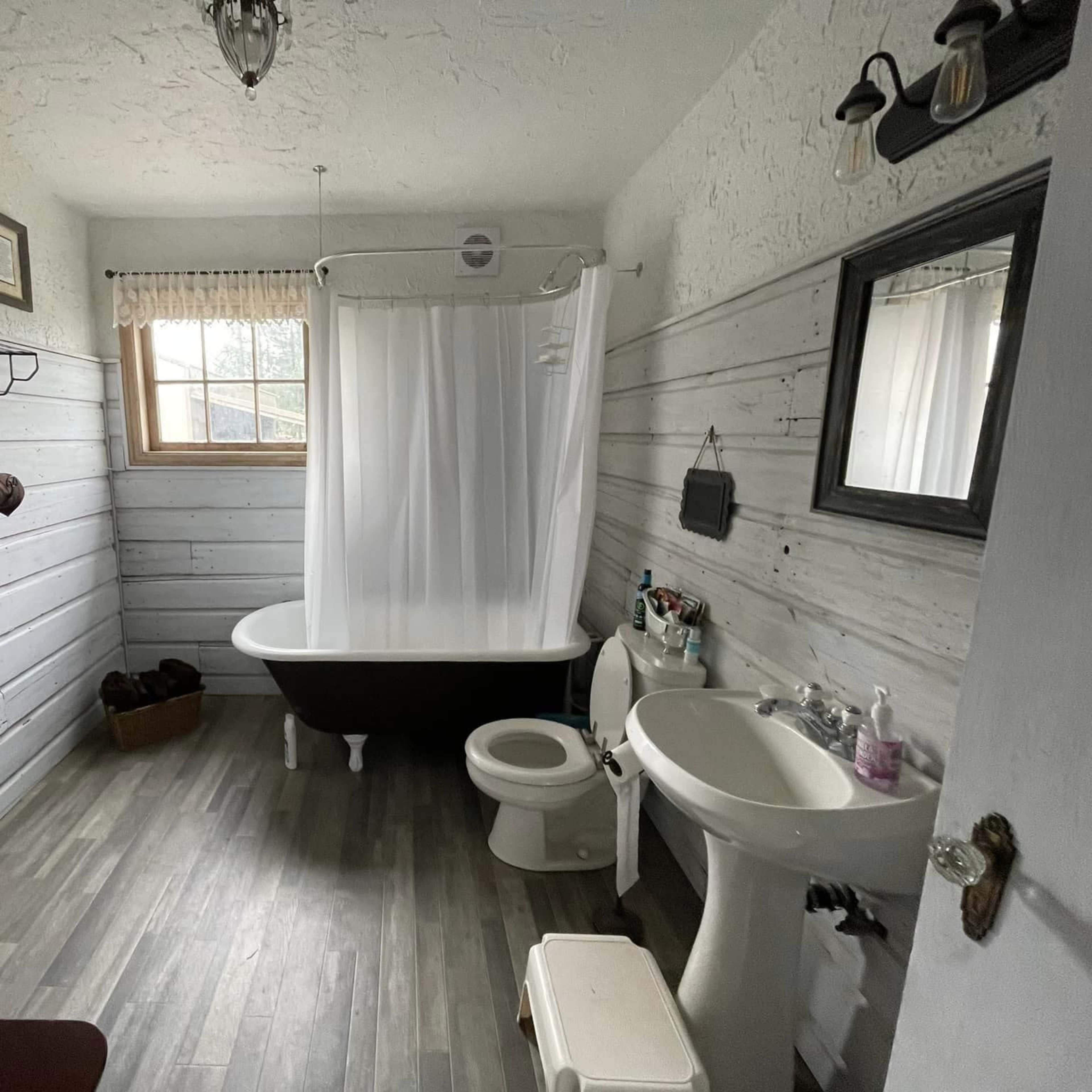 A bathroom featuring a clawfoot bathtub, a toilet, a sink, and wooden paneling on the walls.