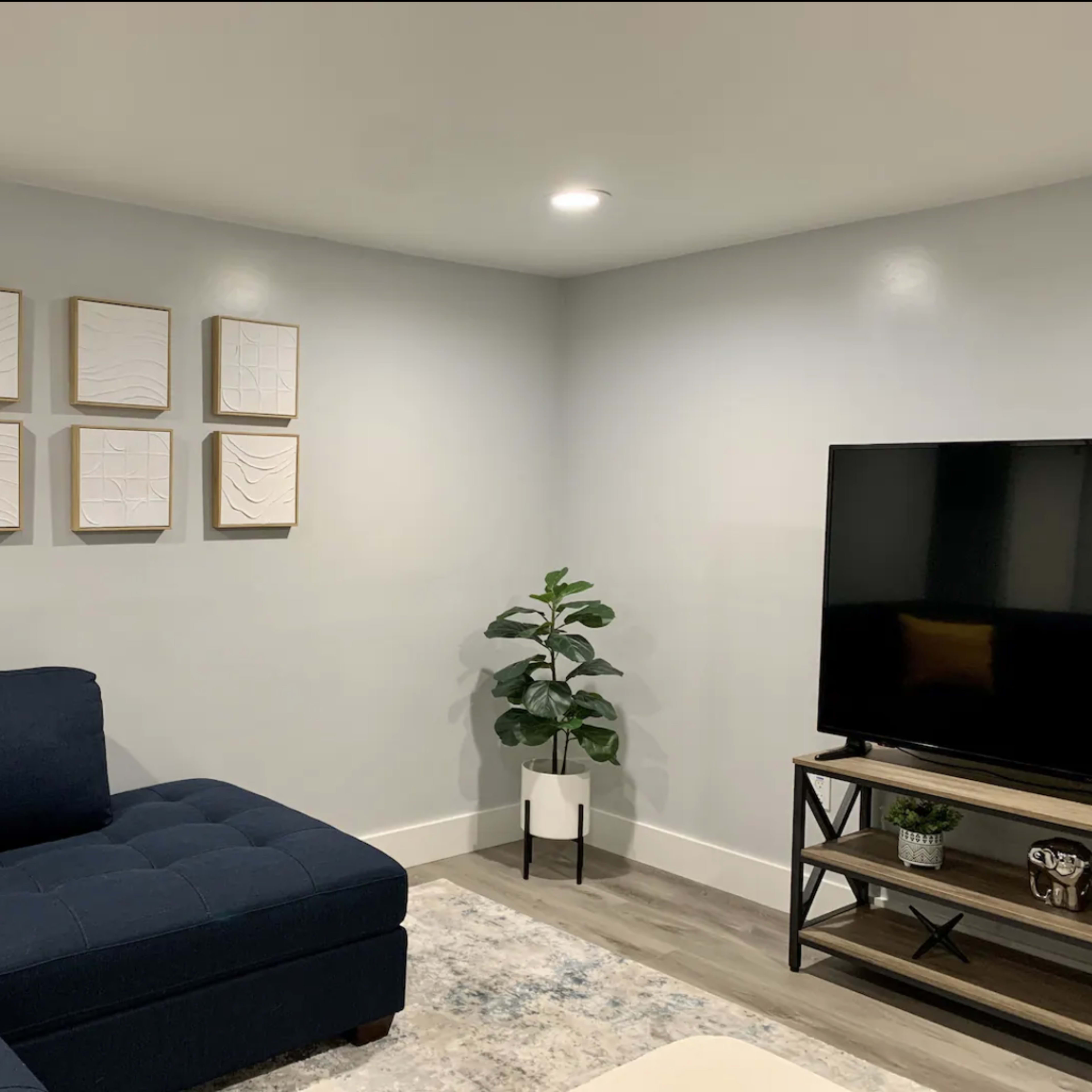 A modern living room with a blue sectional sofa, framed abstract wall art, a television on a stand, and a potted plant in the corner.