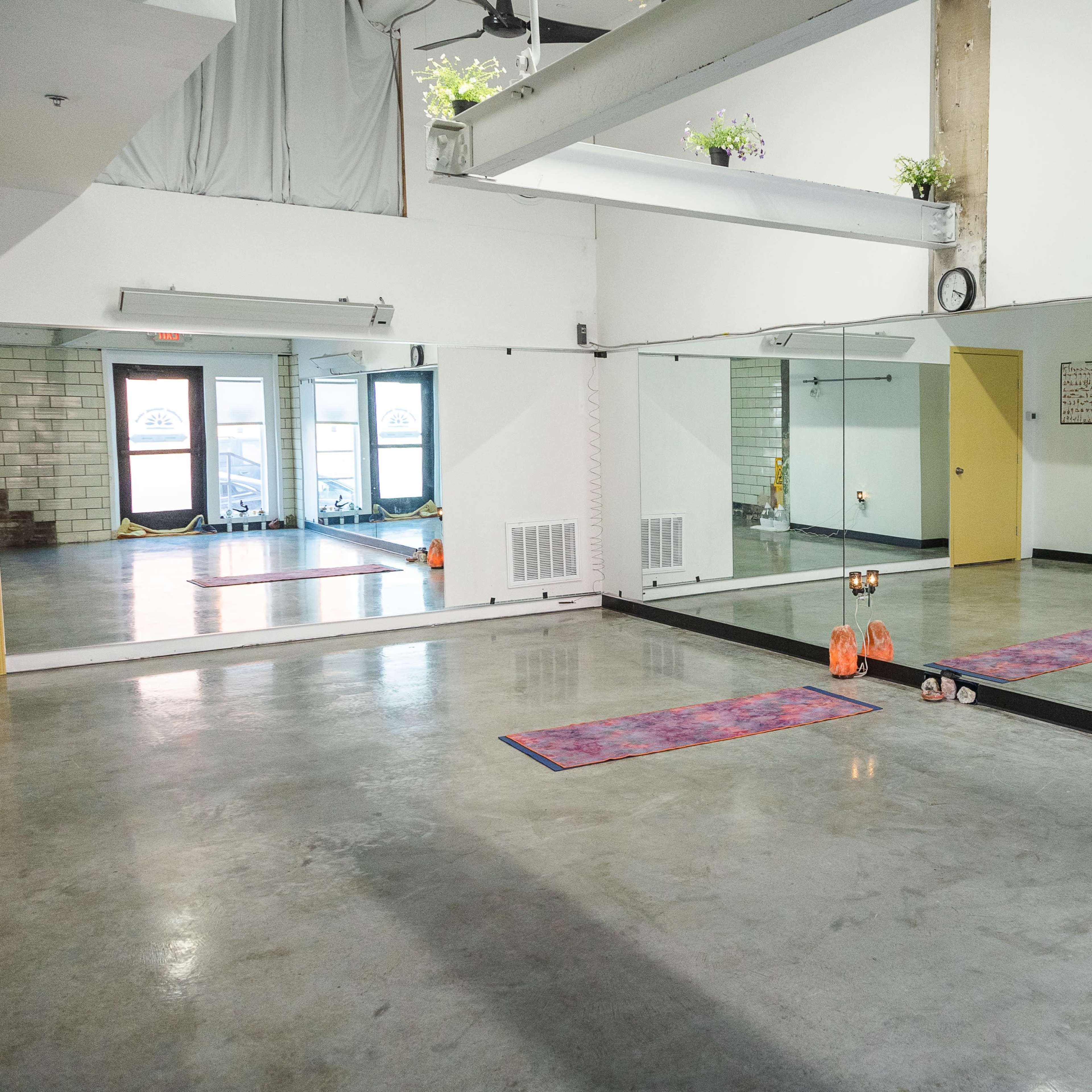 A spacious room with mirrored walls, two exercise mats, and dumbbells on the floor.