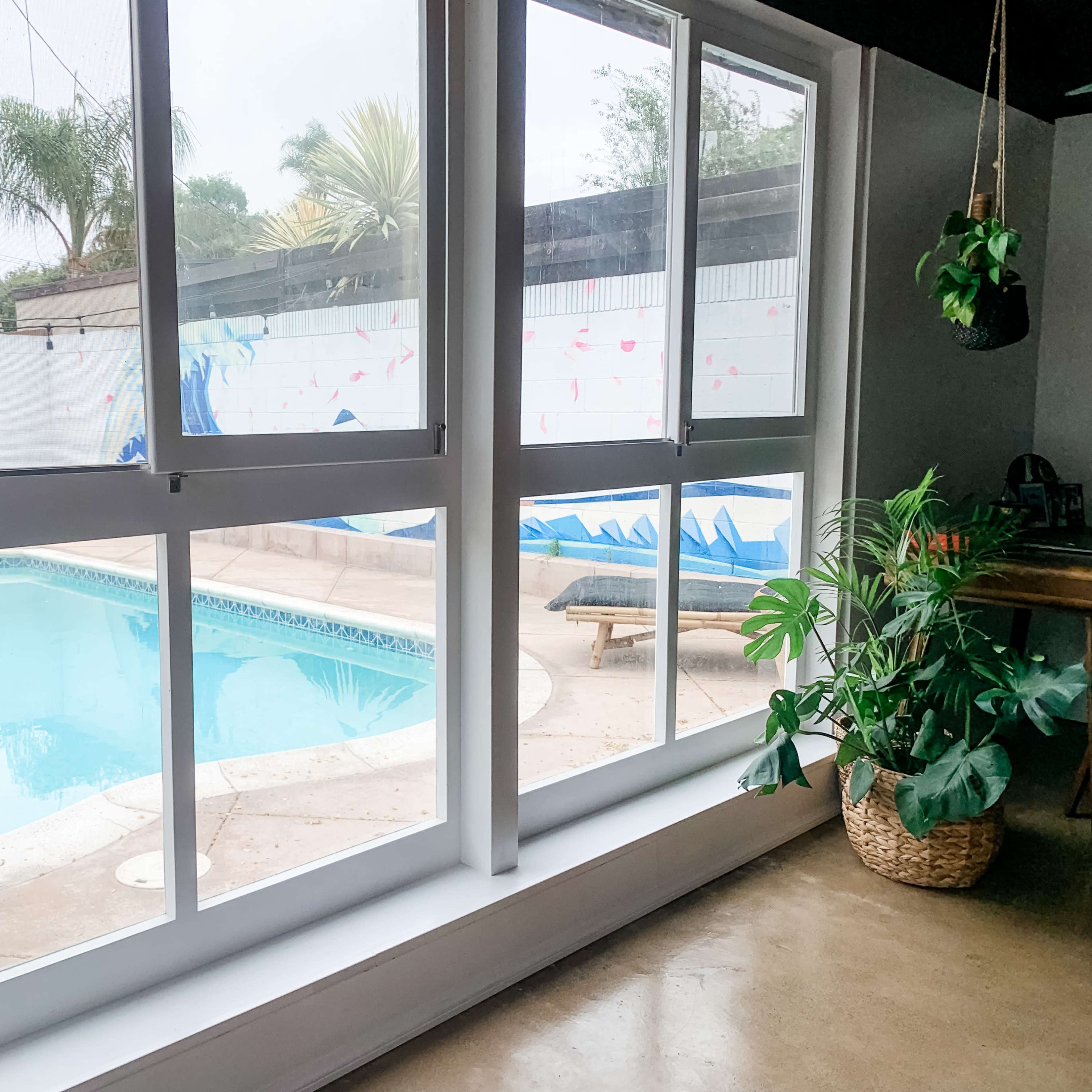 A view of a swimming pool surrounded by a patio, visible through large glass windows.