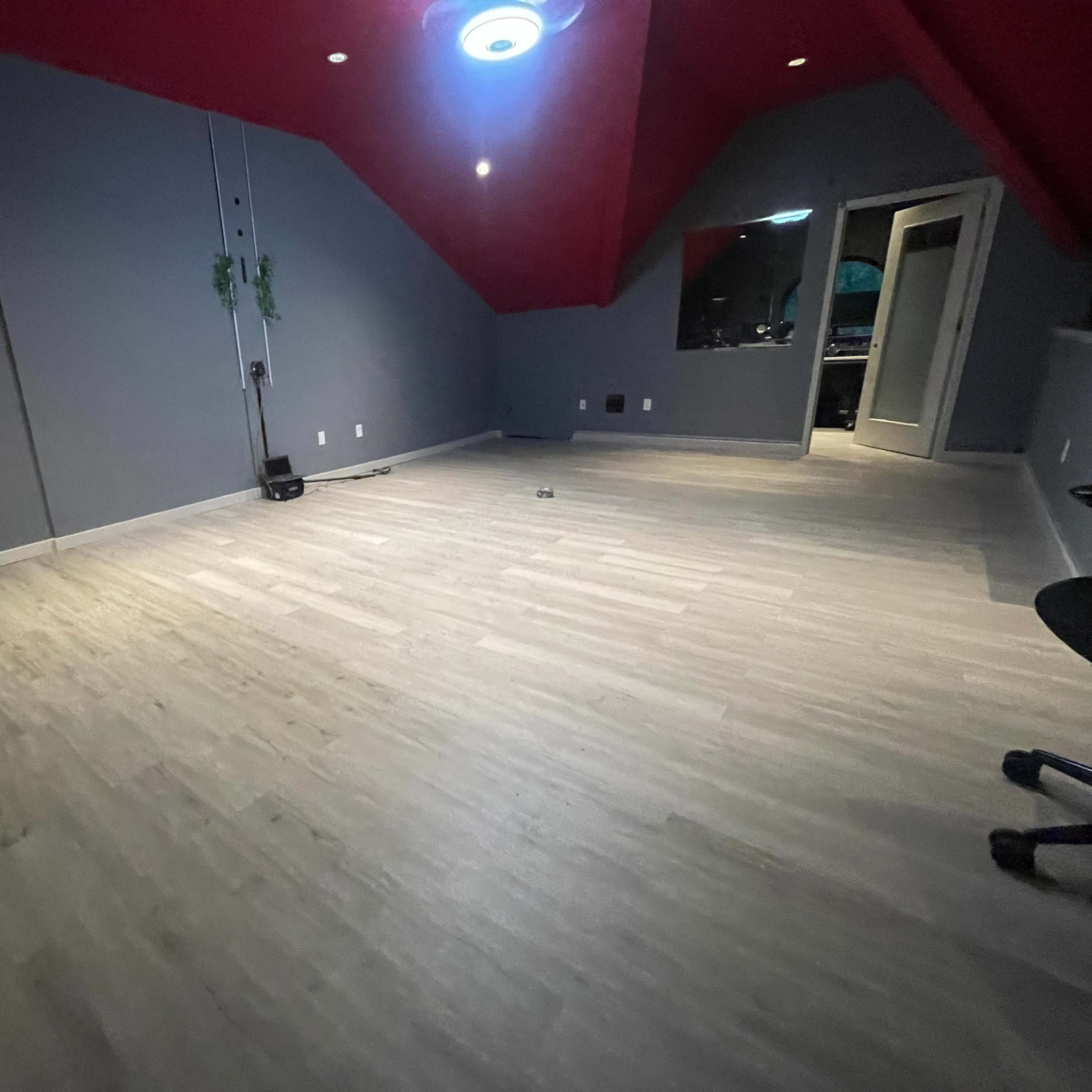 A sparse room with gray walls, red ceiling, and light-colored flooring, featuring a chair in the corner and a door leading to another space.
