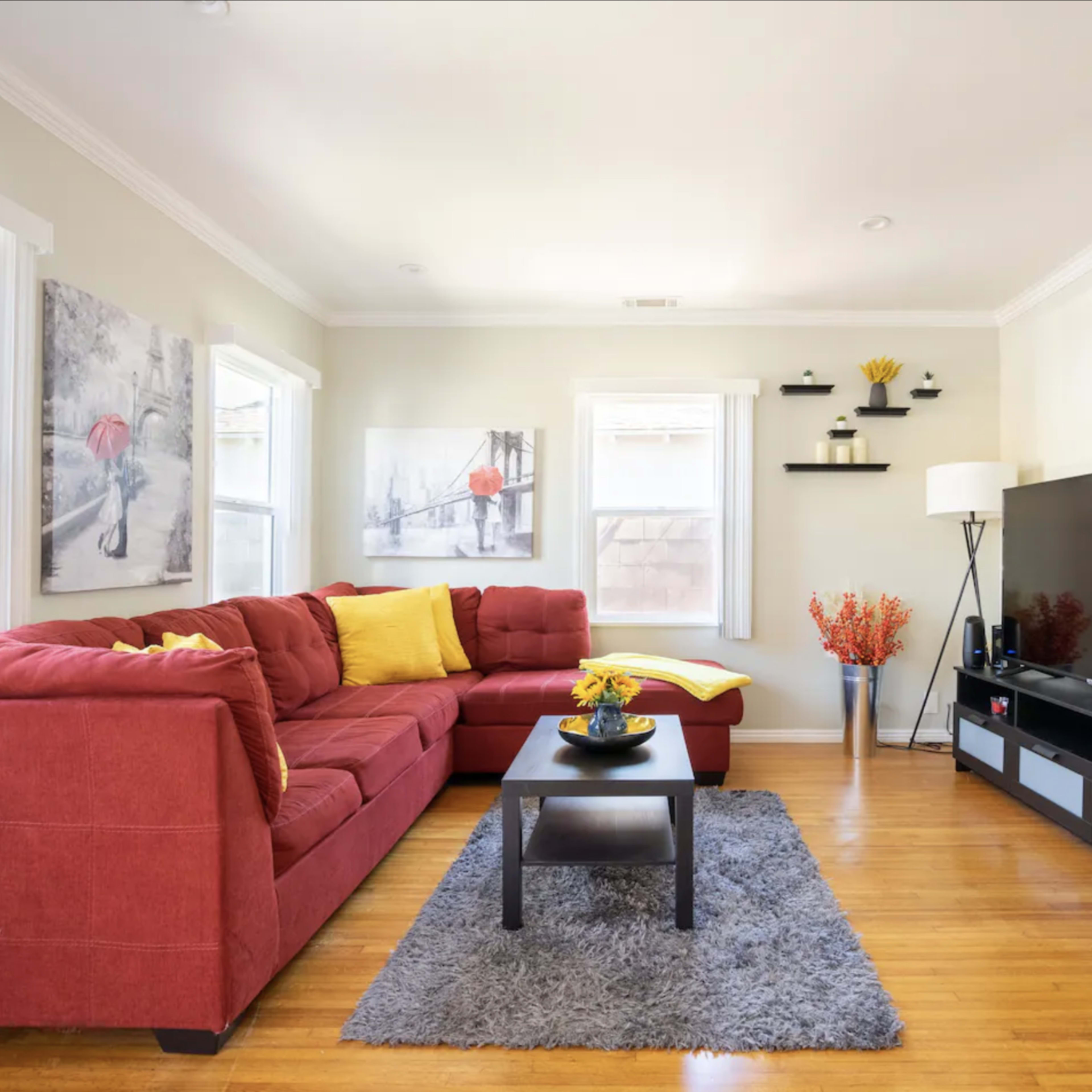 A modern living room with a red sectional sofa, a black coffee table, and a television on a low cabinet against the wall.