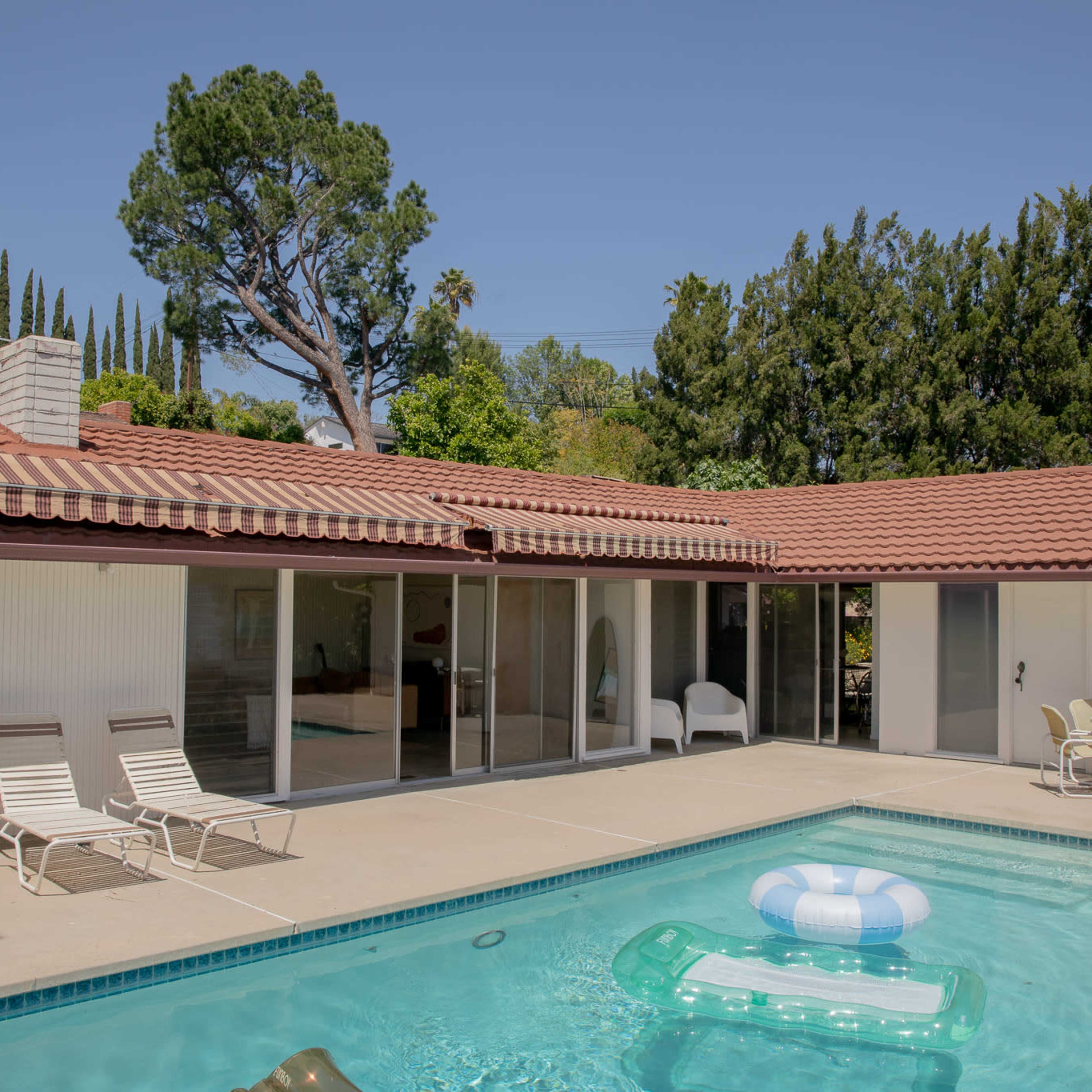 A modern home features a swimming pool with a lounge area and outdoor furniture under clear blue skies.