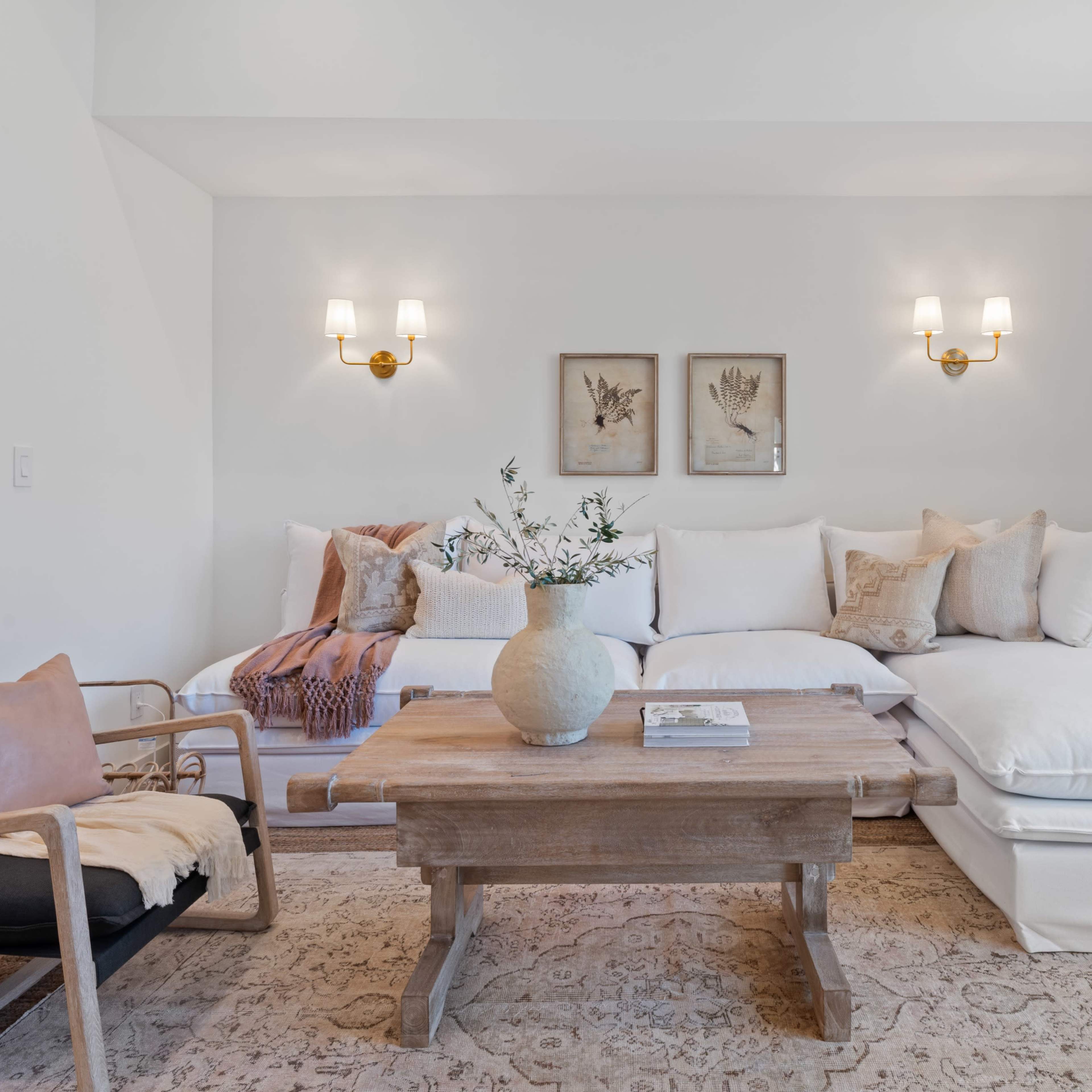 A bright, cozy living room features a sectional sofa with white cushions, a wooden coffee table, and decorative wall art.