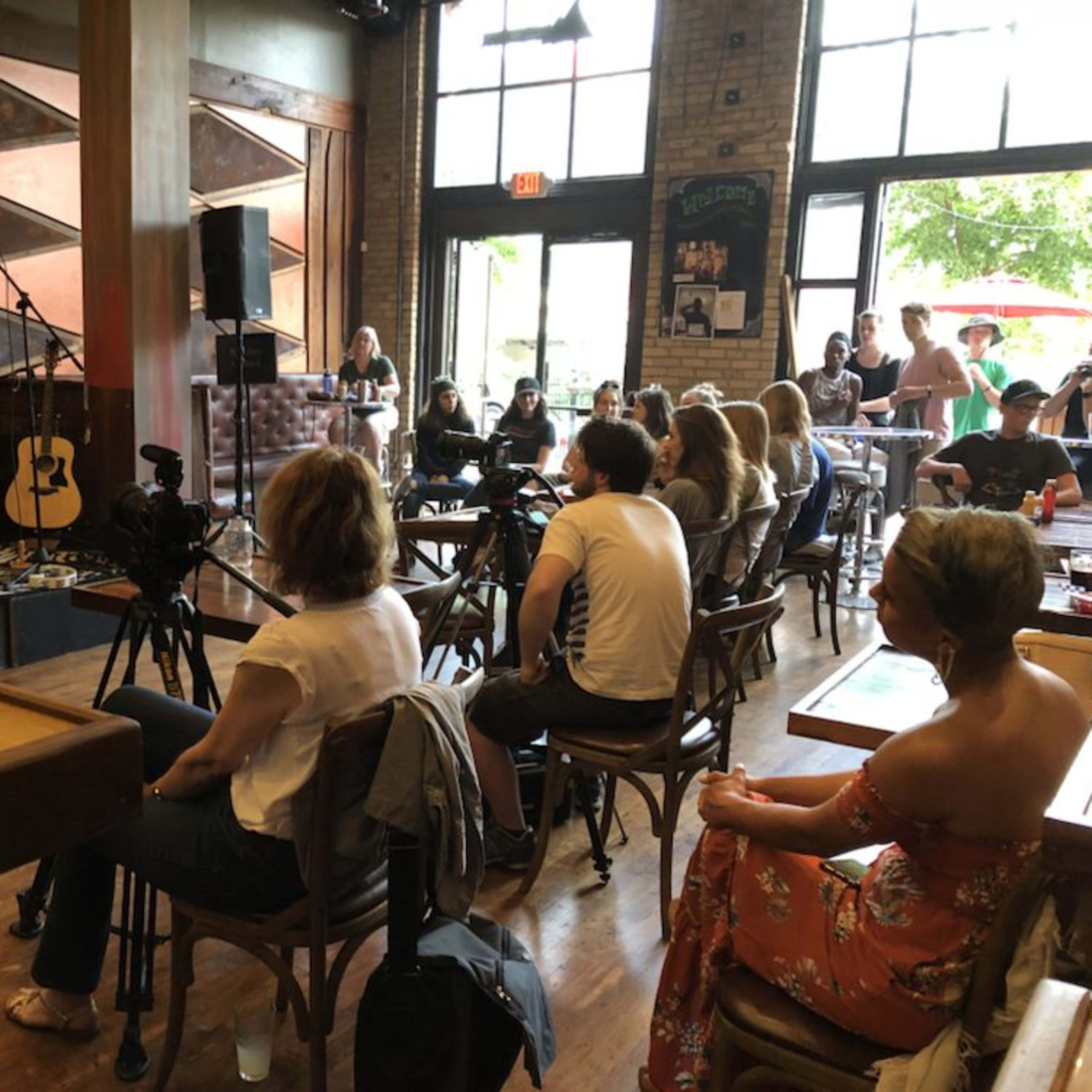 A musician performs on stage in a lively café while an audience observes from seated positions.